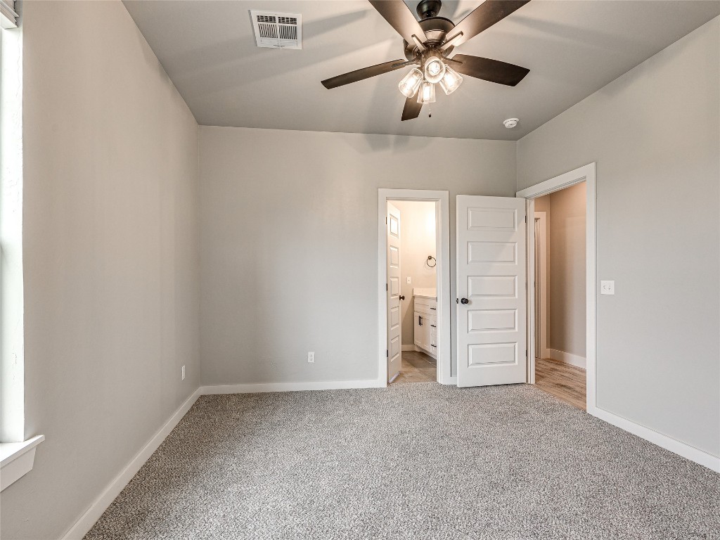 1391 S Kenzie Ct Drive, Mustang, OK 73064 unfurnished bedroom featuring light carpet, ceiling fan, and ensuite bathroom