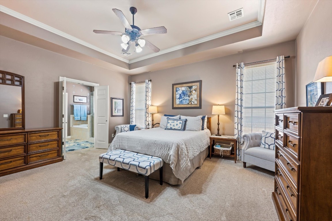 1816 Redland Drive, Edmond, OK 73003 carpeted bedroom featuring ornamental molding, ensuite bath, ceiling fan, and a raised ceiling