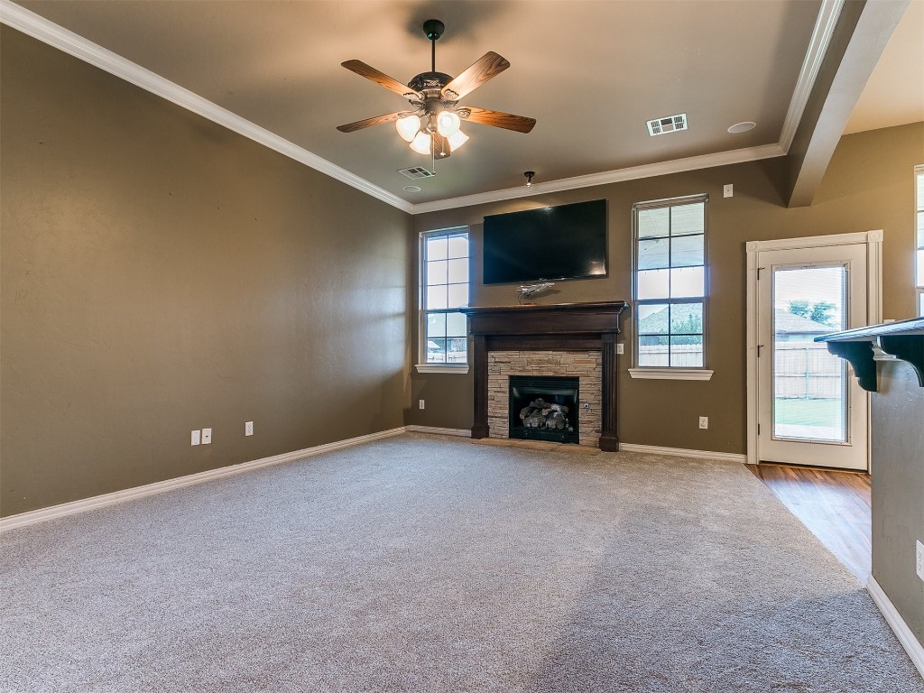 9101 Crooked Creek Lane, Moore, OK 73160 unfurnished living room featuring light carpet, ceiling fan, crown molding, and a fireplace