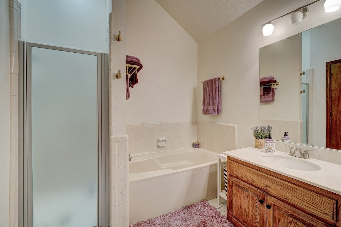 1816 NW 176th Street, Edmond, OK 73012 bathroom with a textured ceiling, vaulted ceiling, vanity, and plus walk in shower