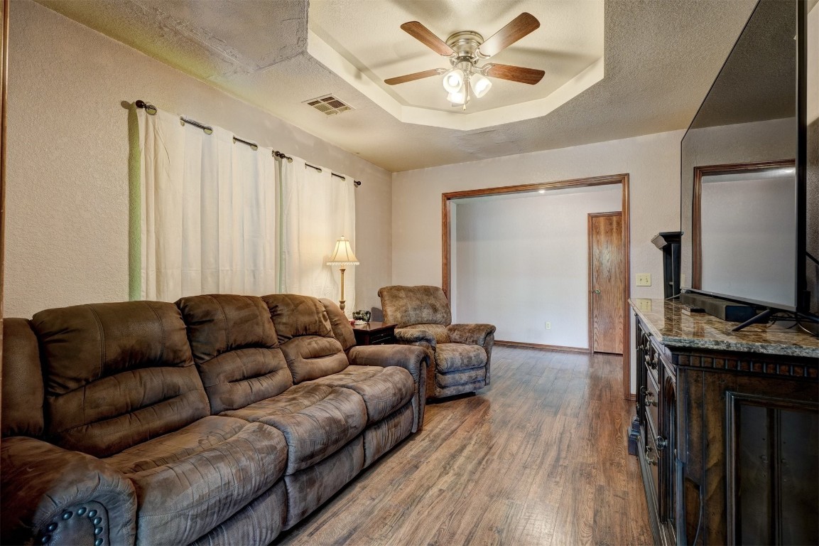 6404 S Peebly Road, Newalla, OK 74857 living room featuring hardwood / wood-style floors, ceiling fan, a raised ceiling, and a textured ceiling