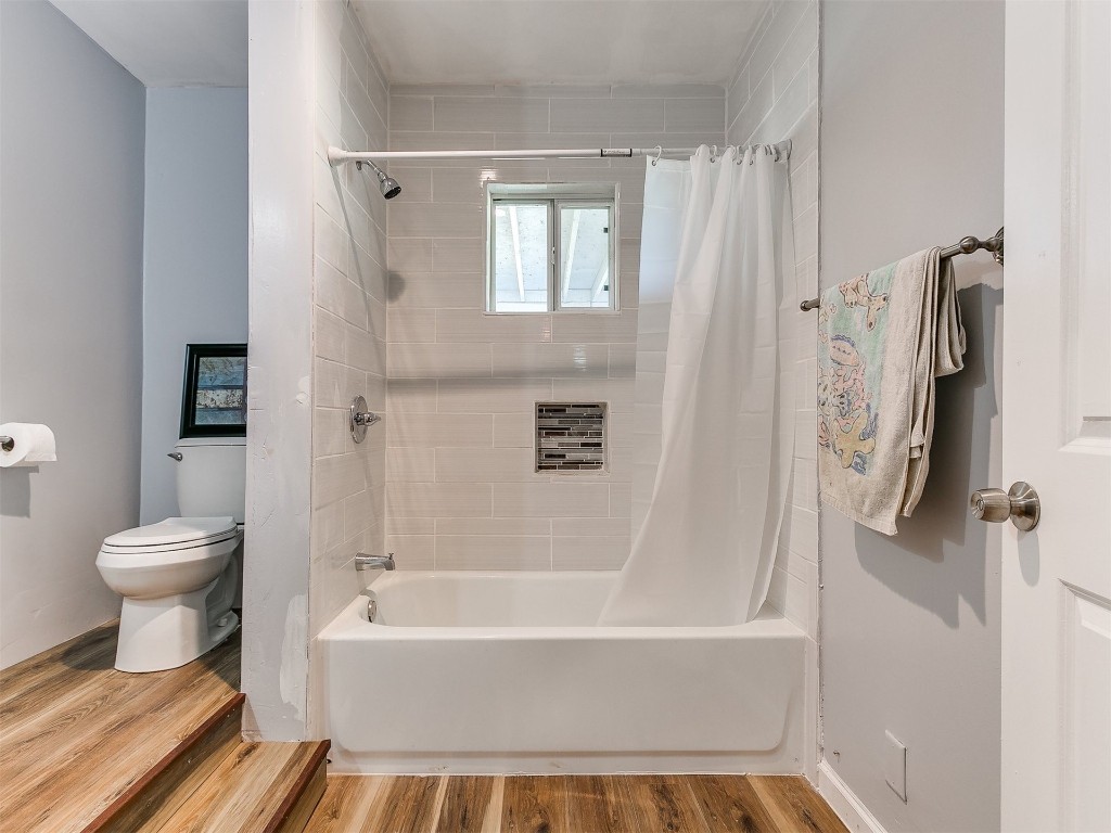 2830 W Georgia Avenue, Chickasha, OK 73018 bathroom featuring wood-type flooring, toilet, and shower / bathtub combination with curtain