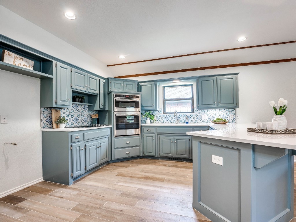 2501 Julies Trail, Edmond, OK 73012 kitchen featuring blue cabinetry, kitchen peninsula, light hardwood / wood-style floors, tasteful backsplash, and stainless steel double oven
