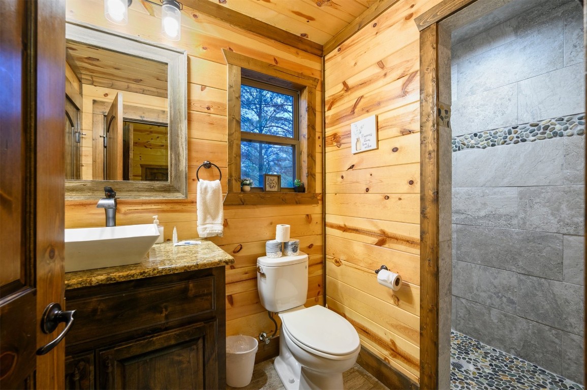 335 Mountain Pine Trail, Broken Bow, OK 74728 bathroom featuring wooden walls, vanity, wooden ceiling, a tile shower, and toilet