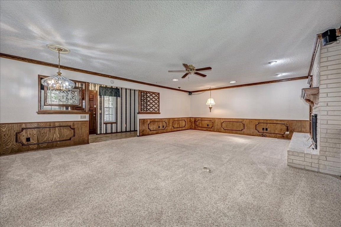923 Rosebrier Court, Guthrie, OK 73044 unfurnished living room featuring a brick fireplace, ceiling fan, crown molding, brick wall, and carpet flooring