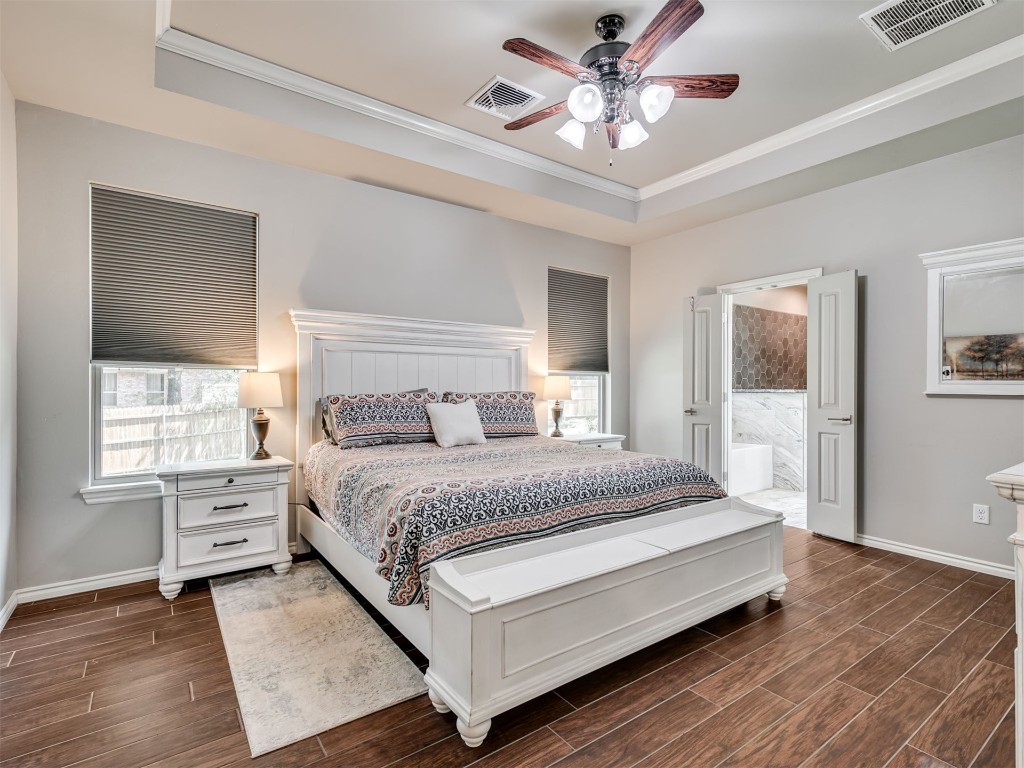 3367 Bobcat Trail, Guthrie, OK 73044 bedroom with ceiling fan, ensuite bathroom, a raised ceiling, dark hardwood / wood-style flooring, and ornamental molding