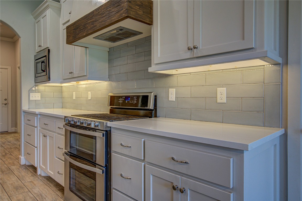 201 Casey Lane, Washington, OK 73093 kitchen with appliances with stainless steel finishes, backsplash, light hardwood / wood-style floors, custom range hood, and white cabinets