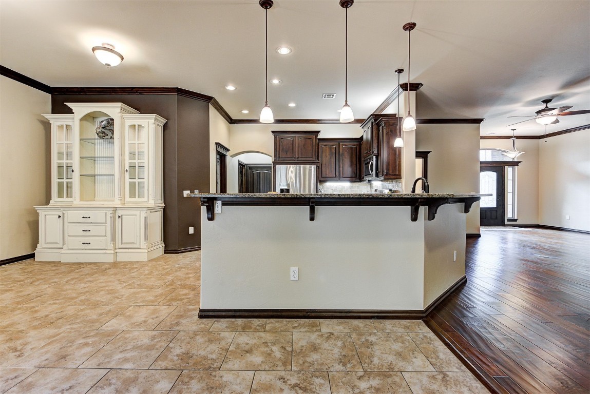 1713 Rain Tree Lane, Choctaw, OK 73020 kitchen with a kitchen bar, ceiling fan, stainless steel appliances, crown molding, and pendant lighting