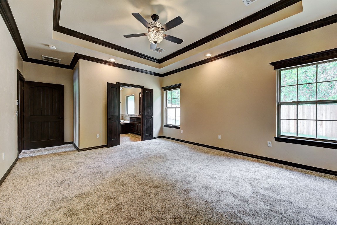 1713 Rain Tree Lane, Choctaw, OK 73020 unfurnished bedroom with ceiling fan, carpet, ensuite bath, a tray ceiling, and ornamental molding