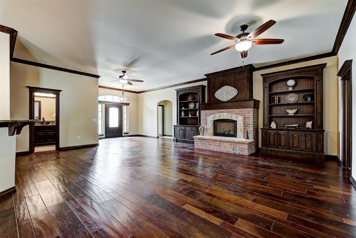1713 Rain Tree Lane, Choctaw, OK 73020 unfurnished living room featuring ornamental molding, dark wood-type flooring, ceiling fan, and a fireplace