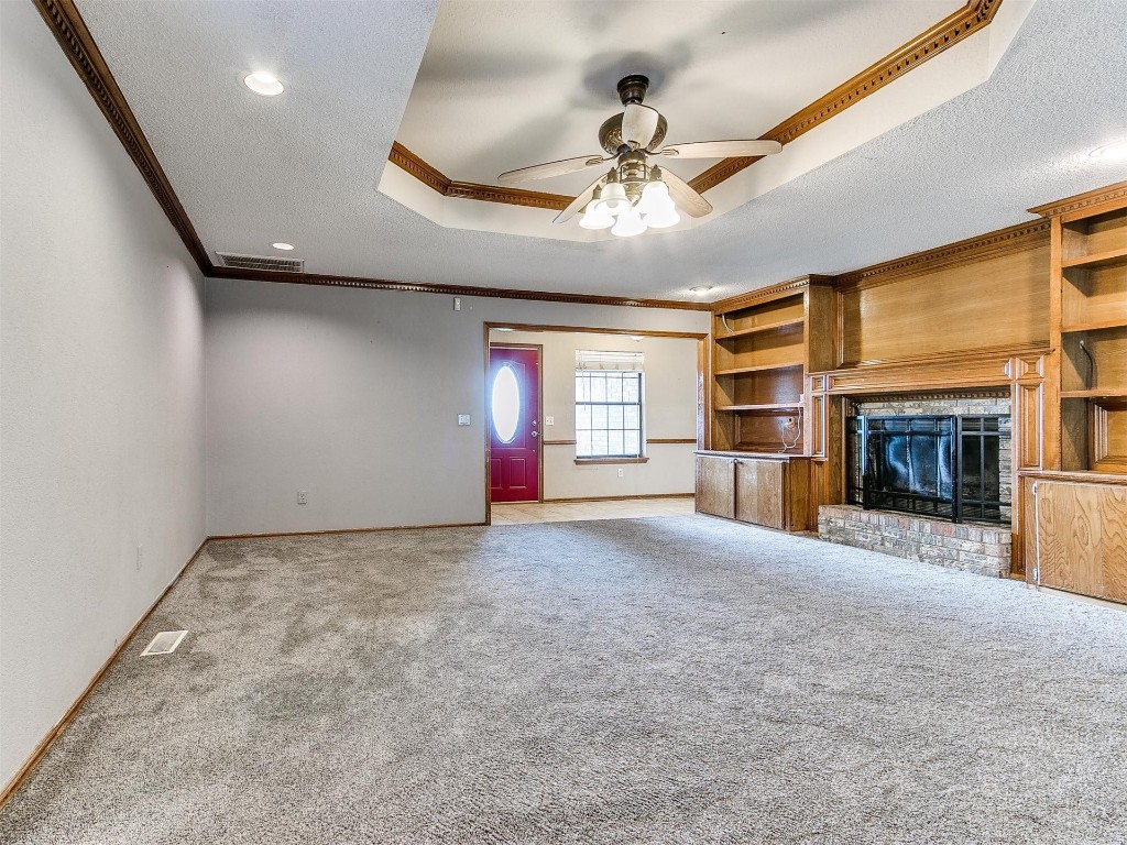 613 Cactus Court, Yukon, OK 73099 unfurnished living room with ceiling fan, crown molding, carpet flooring, a fireplace, and a raised ceiling