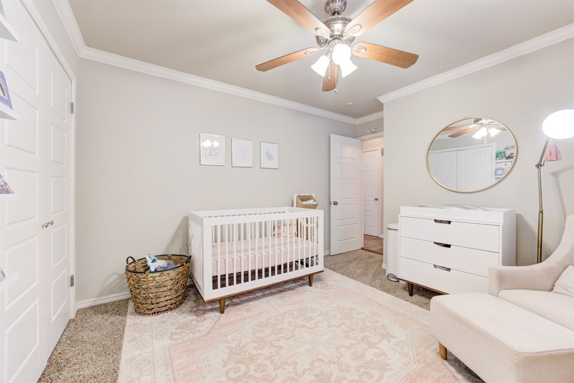 2509 NW 58th Street, Oklahoma City, OK 73112 bedroom featuring ceiling fan, light carpet, a nursery area, and ornamental molding