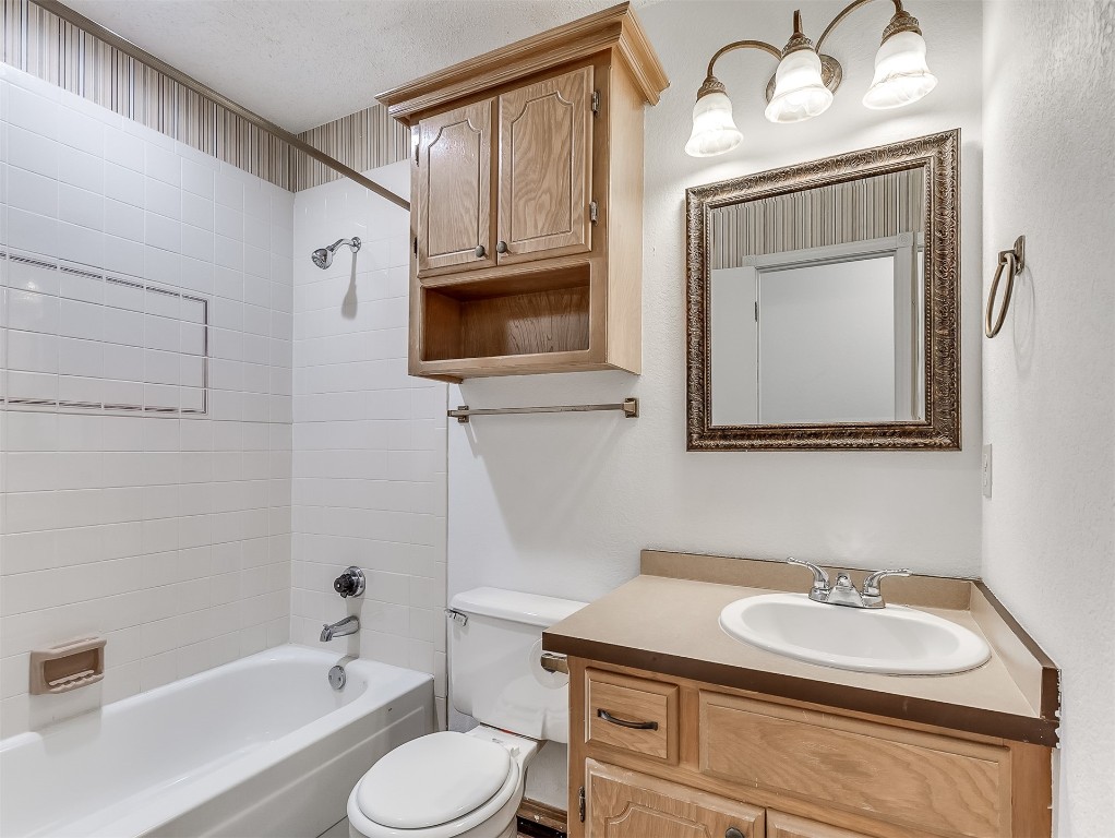 935 W Ridgehaven Way, Mustang, OK 73064 full bathroom with tiled shower / bath combo, a textured ceiling, oversized vanity, and toilet