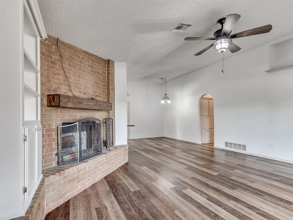 935 W Ridgehaven Way, Mustang, OK 73064 unfurnished living room featuring a fireplace, brick wall, hardwood / wood-style flooring, ceiling fan, and a textured ceiling