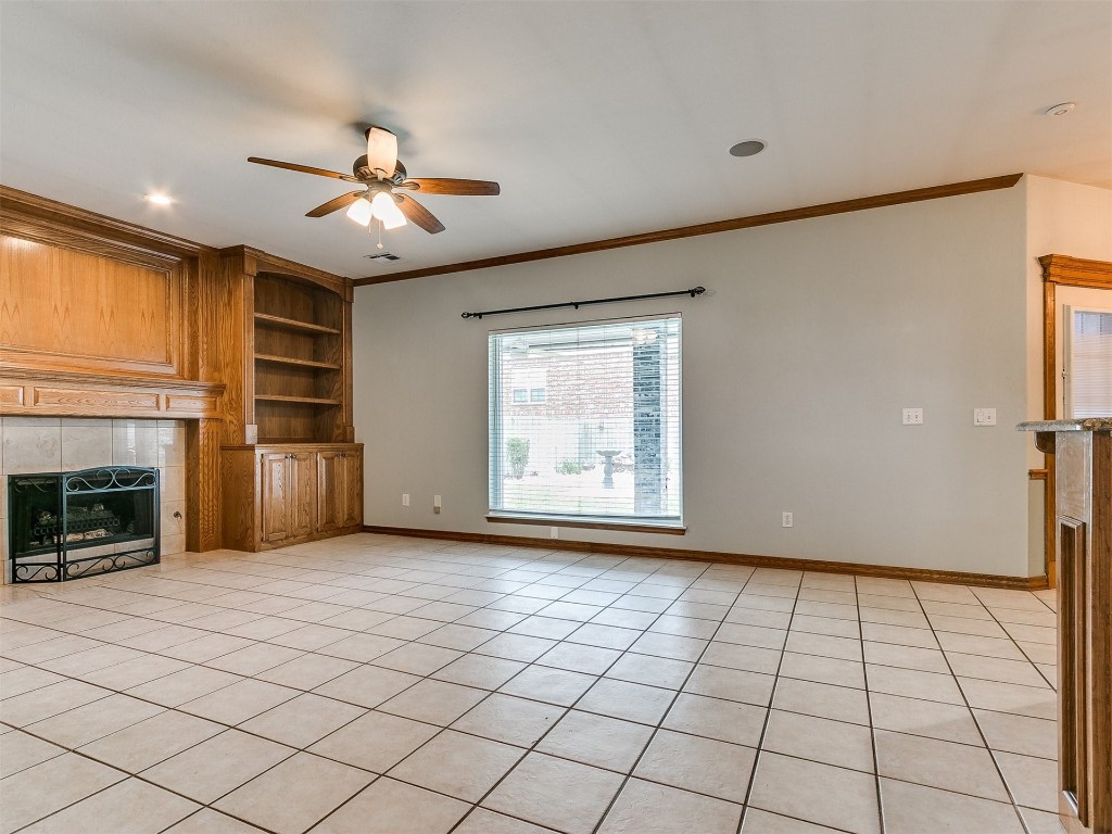 1400 NW 9th Street, Moore, OK 73170 unfurnished living room featuring ceiling fan, crown molding, light tile floors, and a tiled fireplace