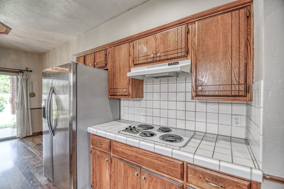 1725 Ryan Way, Edmond, OK 73003 kitchen featuring white gas stovetop, tile counters, tasteful backsplash, dark wood-type flooring, and stainless steel fridge