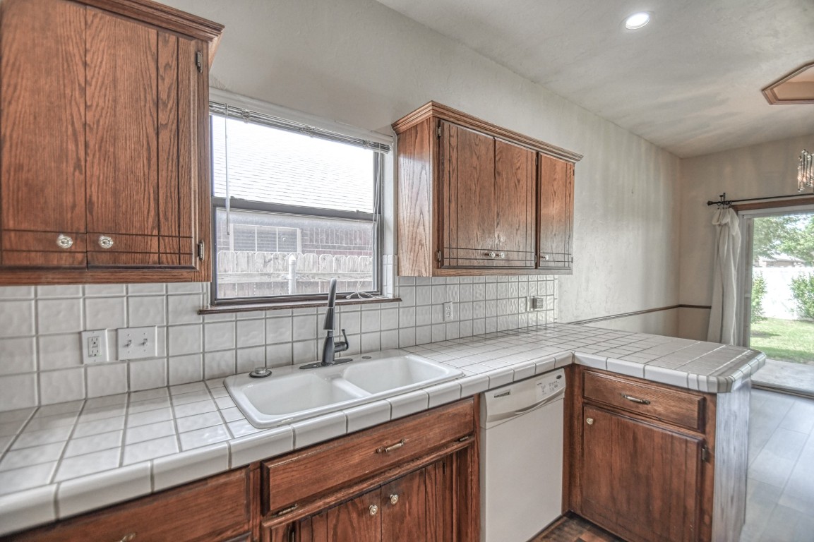1725 Ryan Way, Edmond, OK 73003 kitchen with hardwood / wood-style floors, backsplash, white dishwasher, sink, and tile countertops