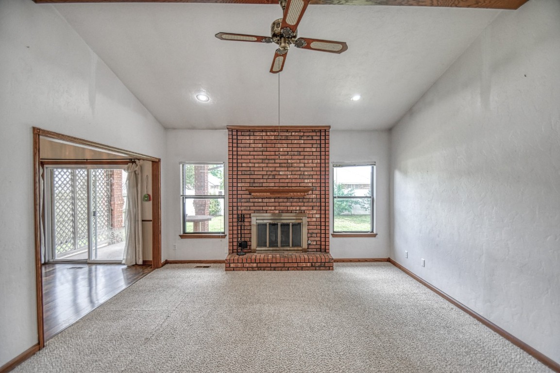 1725 Ryan Way, Edmond, OK 73003 unfurnished living room featuring lofted ceiling, a wealth of natural light, carpet floors, and a brick fireplace