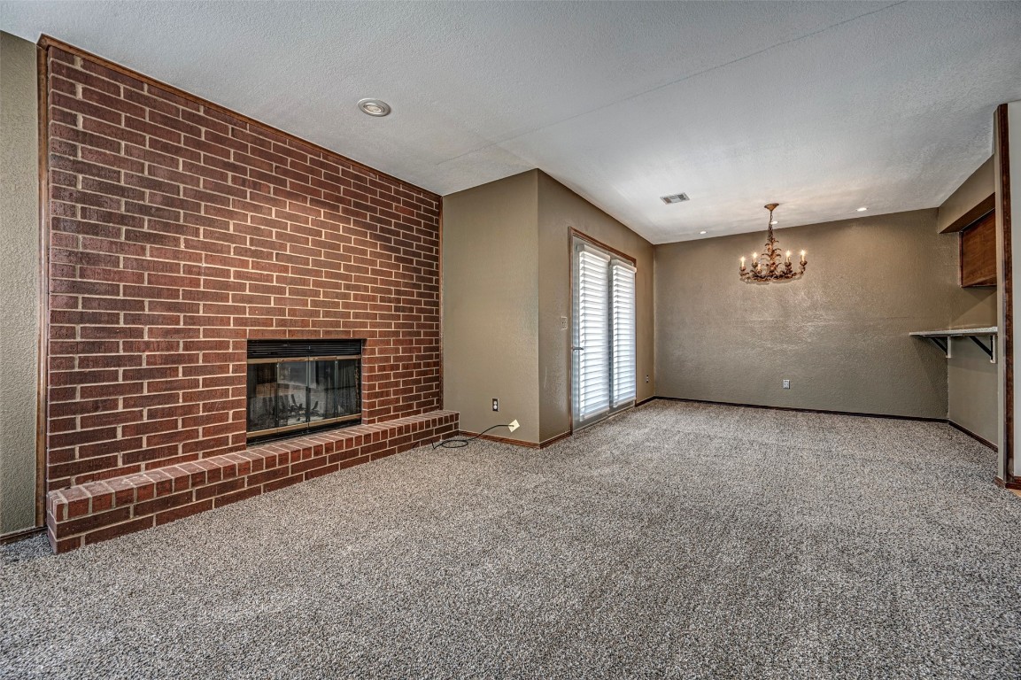 4400 Hemingway Drive, #242, Oklahoma City, OK 73118 unfurnished living room with a textured ceiling, a fireplace, carpet floors, and an inviting chandelier