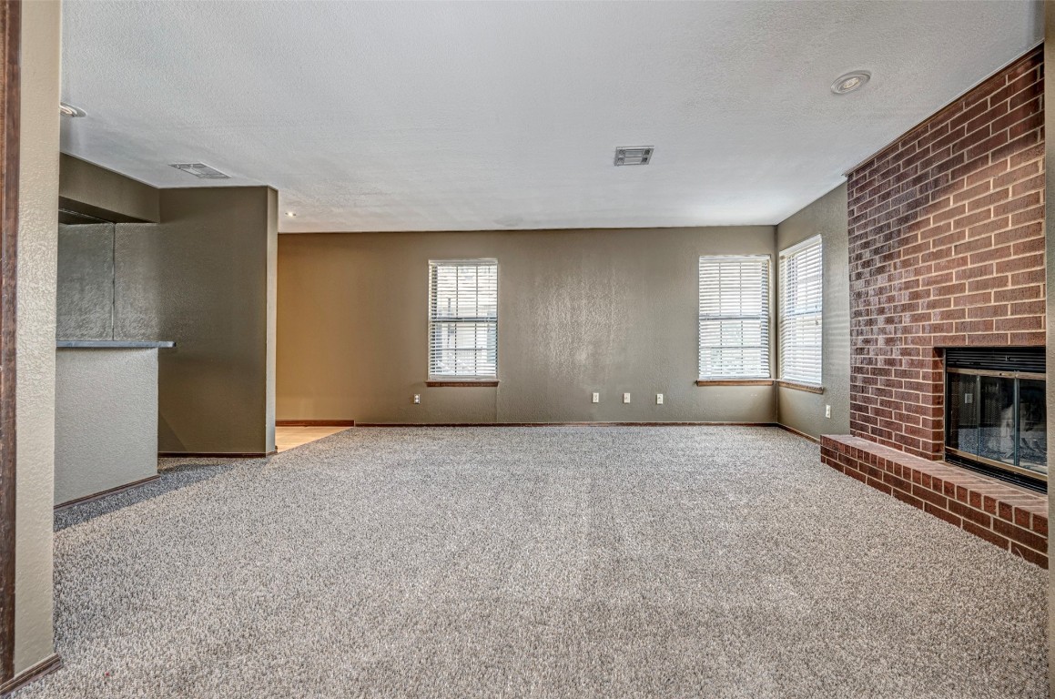 4400 Hemingway Drive, #242, Oklahoma City, OK 73118 unfurnished living room with plenty of natural light, light carpet, a textured ceiling, and a brick fireplace