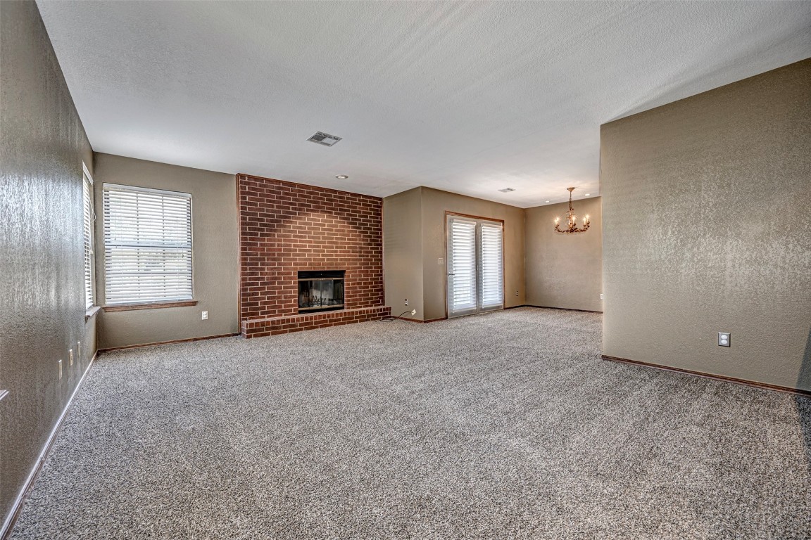 4400 Hemingway Drive, #242, Oklahoma City, OK 73118 unfurnished living room featuring light colored carpet, a notable chandelier, brick wall, and a fireplace