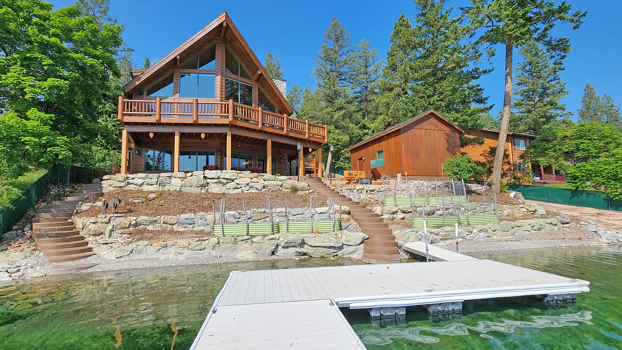 Grand Foys Lake home with lovely north views over aqua waters, Minutes from Kalispell this custom home has a climate controlled boathouse and a rare, private boat launch along 107 ft frontage.  Large windows and cathedral ceiling in the Great Room with rock fireplace enjoys the lake views. An ample kitchen has room for more than one cook, or use the 2nd kitchen in the lower level to feed a crowd. Entertain on the deck or lower patio overlooking the lake! Top floor loft is solely the primary bedroom suite overlooking the great room and has large bath with soaking tub, shower and roomy closet. Home was designed to add an elevator reaching all 3 levels if desired. Finishing the home are a lower Family Room, two more bedrooms and a bonus room, two laundry areas.  Private gate enters onto the concrete driveway, property is fenced and has alarm system. Short drive to Herron Park and within an hour from Flathead Lake, Glacier National Park and skiing at Whitefish Mountain Resort.