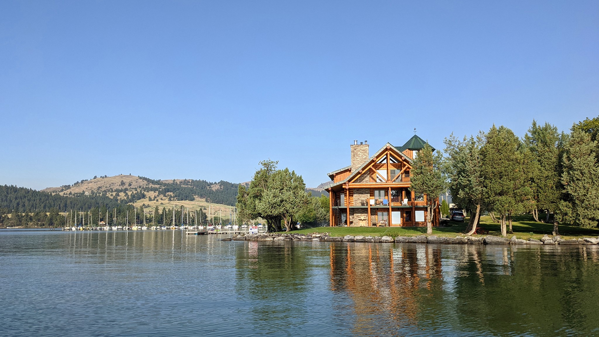 Absolutely lovely log home set at waters edge with Flathead Lake 202 ft frontage facing east and south mid point on the westshore in Dayton. Spacious main floor living with huge windows light up the Great Room with stone fireplace, gourmet Kitchen & Dining. Big wrap deck area makes for a great spot to take in the lake views with many sailboats in the area. The Primary Bedroom suite adjoins an enclosed Hot Tub room overlooking the south frontage and dock. Full lower level enjoys Family Room with 2 seating areas, game area and alcove, lovely guest bedroom and bath; Walk out to patio and to grassy lawn.  Upstairs is loft library space, two more bedrooms and full bath. The darling caretaker or guest apartment is across the west patio and adjacent to double Garage. East and South views of the Mission Range & Wild Horse Island.  Call Scott Hollinger at 406-253-7268 or your real estate professional.