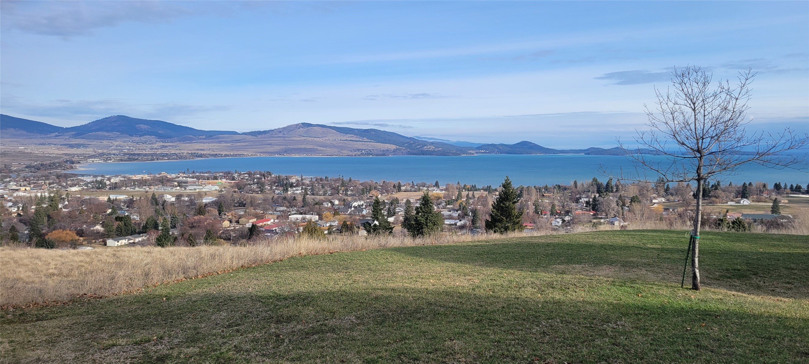 Few areas close-in to downtown offer quietude as well as superior views atop the sleepy town of Polson and across the an amazing expanse of Flathead Lake.  From this elevated and sunny location, the Mission Range is also quiet dramatic.  Claffey Drive is not a through street, but convenient to down town, as old town is about a mile, via safe walking trails on Skyline Drive into town and also miles south.  The land corridor that shoulders the northerly boundary is teeming with wildlife.  This place has large, mature deciduous trees, lilac stands, shrubs /flowers, and a fenced in back yard. Decks front and back, daylight walk out basement, fireplaces up and down, new roof,  detached double garage, paved drive. Traditional 80's style home.  It is dated, but with good bones, new roof, and a wood burning fireplace, rendering it a fierce contender in its price range.
