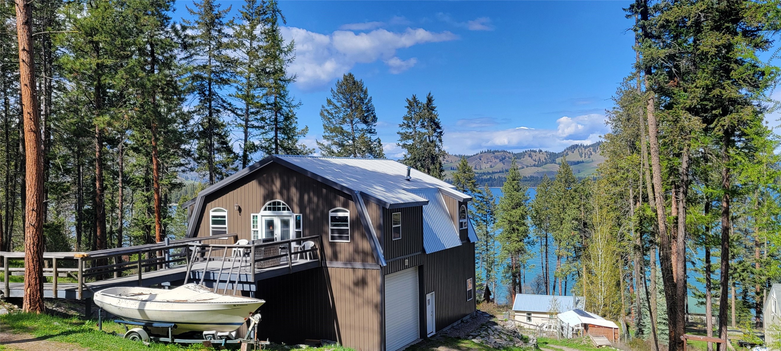 Special 3 season destination property, having deeded common lake access to boat and play on Flathead Lake. Views through the trees to Dream Island, with lots of potential to personalize your own scene. Newer shop with living quarters plus an original 1 bedroom cabin on a 3.7 ac. lot just 15 minutes north of Polson. The "shouse" 1st level has a 12'hi overhead door, work shop consists of 50% of that level w 220 A/S. Remainder of ground floor has 1BR, 1Ba, and a sunroom. Upper (main floor) combines beautiful vaulted ceilings, custom cabinetry and woodworks, a wet bar, dining area, kitchen w propane range, subzero refrigerator, freezer. 1 main floor bedrm, a3/4 ba, laundry & bonus room, w free standing oil stove, and glass  doors. Fronting Melita Isl Rd, a charming renovated 1930 cabin w plank wood floors, kitchen, 3/4 Ba, covered sitting porch. Great Rental hs. Many personal affects in "shouse" can be included, negotiated, or moved. Shared engineered septic system,  Shared private well.
