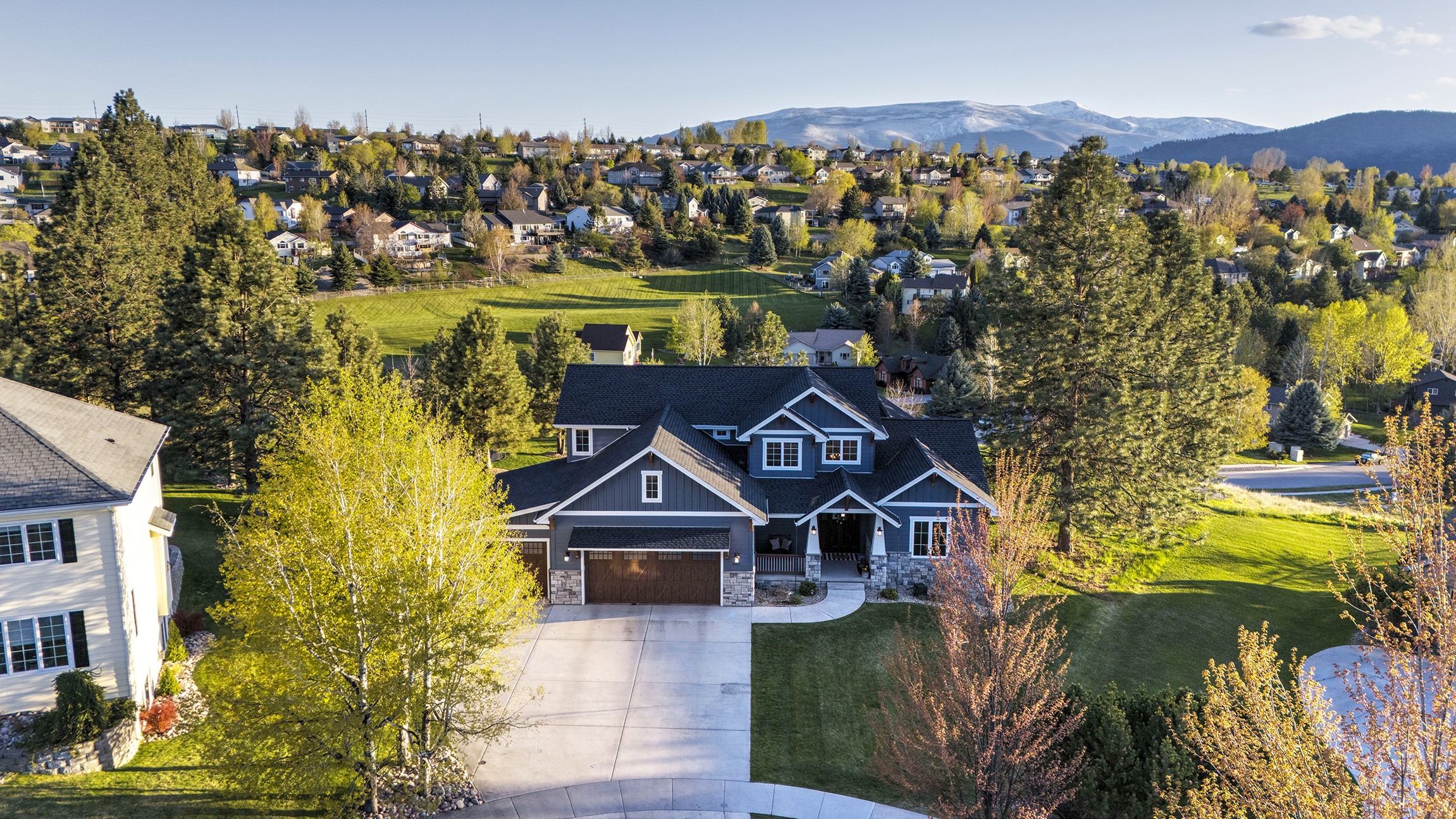 Nestled in Upper Miller Creek, this residence spans over 5,600+ square feet on a generous 0.89 acre lot situated at the end of a cul-de-sac. Crafted by Hoyt Homes in 2017, this custom home opens to breathtaking views of the mountains and Missoula Valley. The home features an inviting open layout encompassing the dining room, living space, and kitchen, with custom shelving around a rock fireplace, and custom cabinets in the kitchen. Natural light floods into the living room that is accentuated by substantial wooden beams and lofty ceilings, while the kitchen boasts a Bosch Appliance package inclusive of double ovens, built-in microwave, dishwasher, and gas stove top. The expansive island features a farmhouse sink and quartz countertops. With double sliders opening to the sizable trex deck, the dining room is a welcoming space. Adorned with hardwood flooring in key areas on the main level, the foyer boasts soaring vaulted ceilings. A sliding barn door opens to the pantry, complete with plumbing for an ice maker. The laundry room offers shelving, cabinets, and a sink, while the mudroom comprises of six custom lockers and ample storage, that is adjacent to a home office. The primary suite features a slider to the back deck, an on-suite walk-in closet, and a luxurious bathroom with double sinks, tile floors, a sizable soaker tub, tile shower, and a private water closet. A guest bedroom and bath are located near the entrance, with the bath showcasing tiled floors and a shower. Upstairs, a loft area and two spacious bedrooms with en-suite bathrooms, vanity areas, and generous closets await. The lower level hosts a generous family room with sliders to the lower patio, featuring a convenient drinking fountain nearby. The bar area boasts a sink, brick backsplash, granite counters, a mini fridge, and a microwave oven. The gym, equipped with an egress window and ample closet space, could double as a bedroom. Two additional bedrooms, a full bath, and a half bath are also included downstairs. The utility room houses a secondary set of washer and dryer hookups, the zoned boiler system, and the central air conditioning. The home benefits from radiant floor heating with ten distinct zones. Outside, the yard offers a shed, a fenced garden area, a rock fire pit, in-ground trampoline, and a triple-car garage. Bordering city open space, this property will forever have unobstructed views and privacy. 2831 Carla Jo Lane offers a serene and luxurious living experience in Missoula, MT. Contact Kris Hawkins, 406-396-6542, or your real estate professional today.