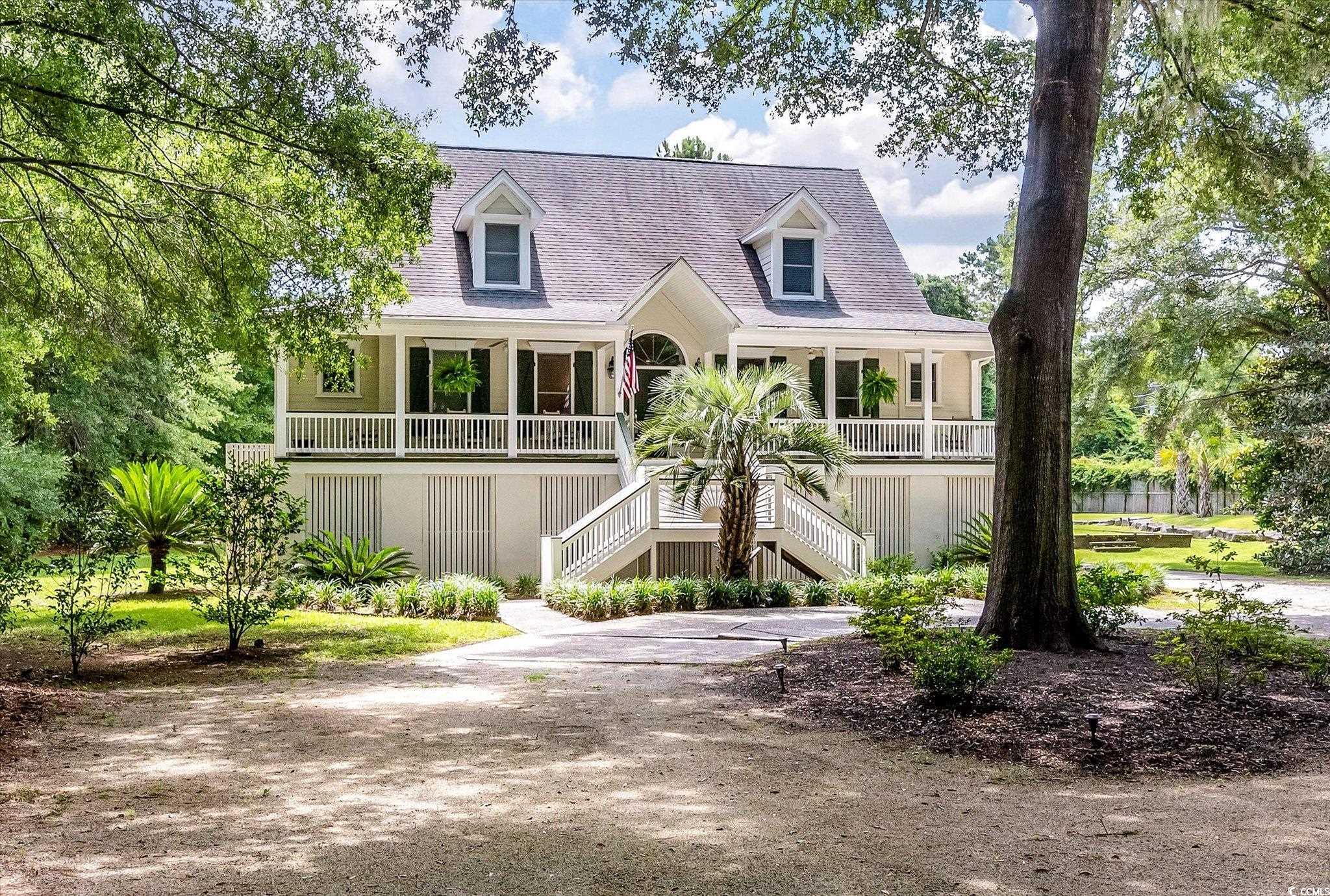 Raised house with a long covered porch, central staircase, and mature trees.