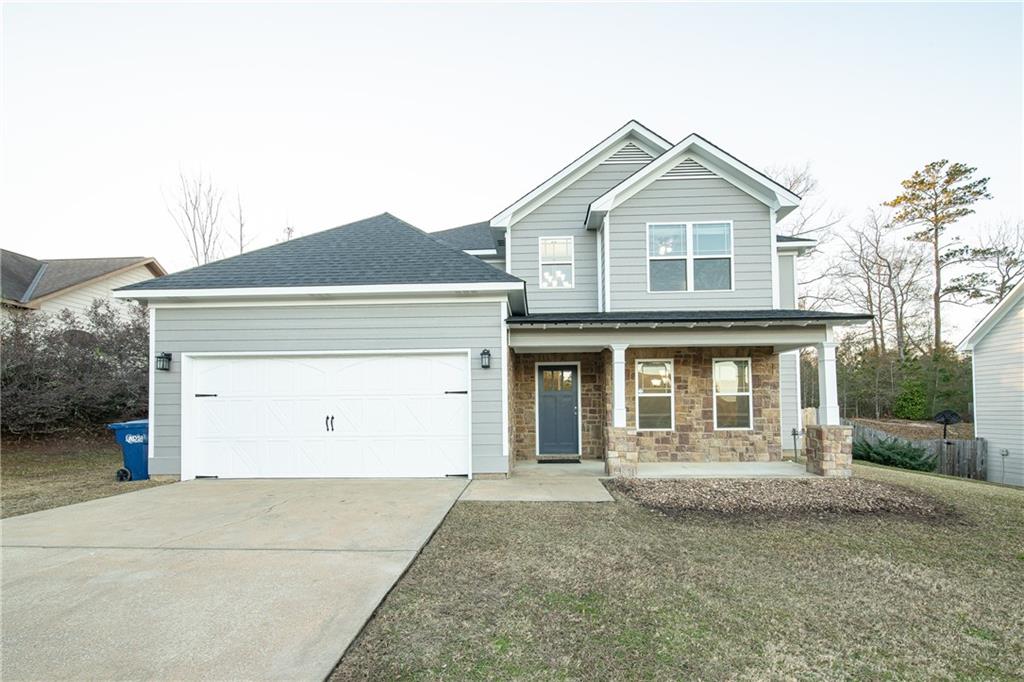 Two-story gray home with stone facade, covered porch, and wide concrete driveway.