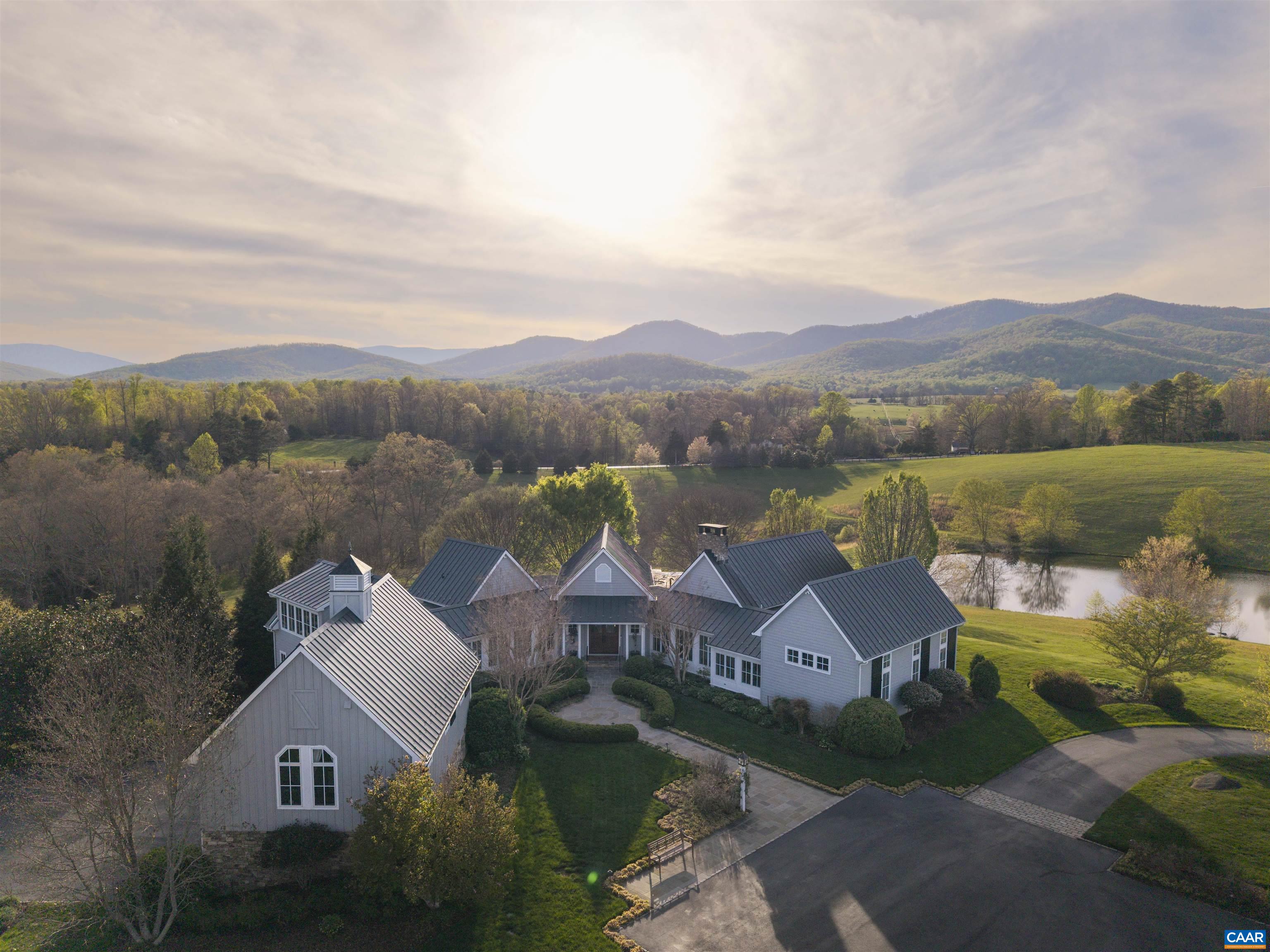 Grey Oaks is a magnificent 53-acre estate in Free Union, offering total privacy and stunning views of the Blue Ridge Mountains. Rolling meadows, mature oaks, tranquil streams, and two ponds—one stocked—create a breathtaking landscape. The custom-built residence by Shelter Associates boasts six bedrooms, six-and-a-half baths, and superb craftsmanship. A soaring great room with exposed beams and a fireplace anchors the home, complemented by a chef’s kitchen, elegant dining and breakfast rooms, and a cozy paneled den. The light-filled primary suite enjoys a private wing with his & her bathroom, while a separate three-bedroom guest/in-law retreat features a full kitchen, dining area, and loft-style family room with a fireplace. Extensive porches, a three-bay garage, an 1,800± sq. ft. barn, and no conservation easement enhance the property’s appeal. Walking trails, a charming creekside bridge, and raised garden beds complete this extraordinary offering. Only 15 miles NW of Charlottesville and the University of Virginia.