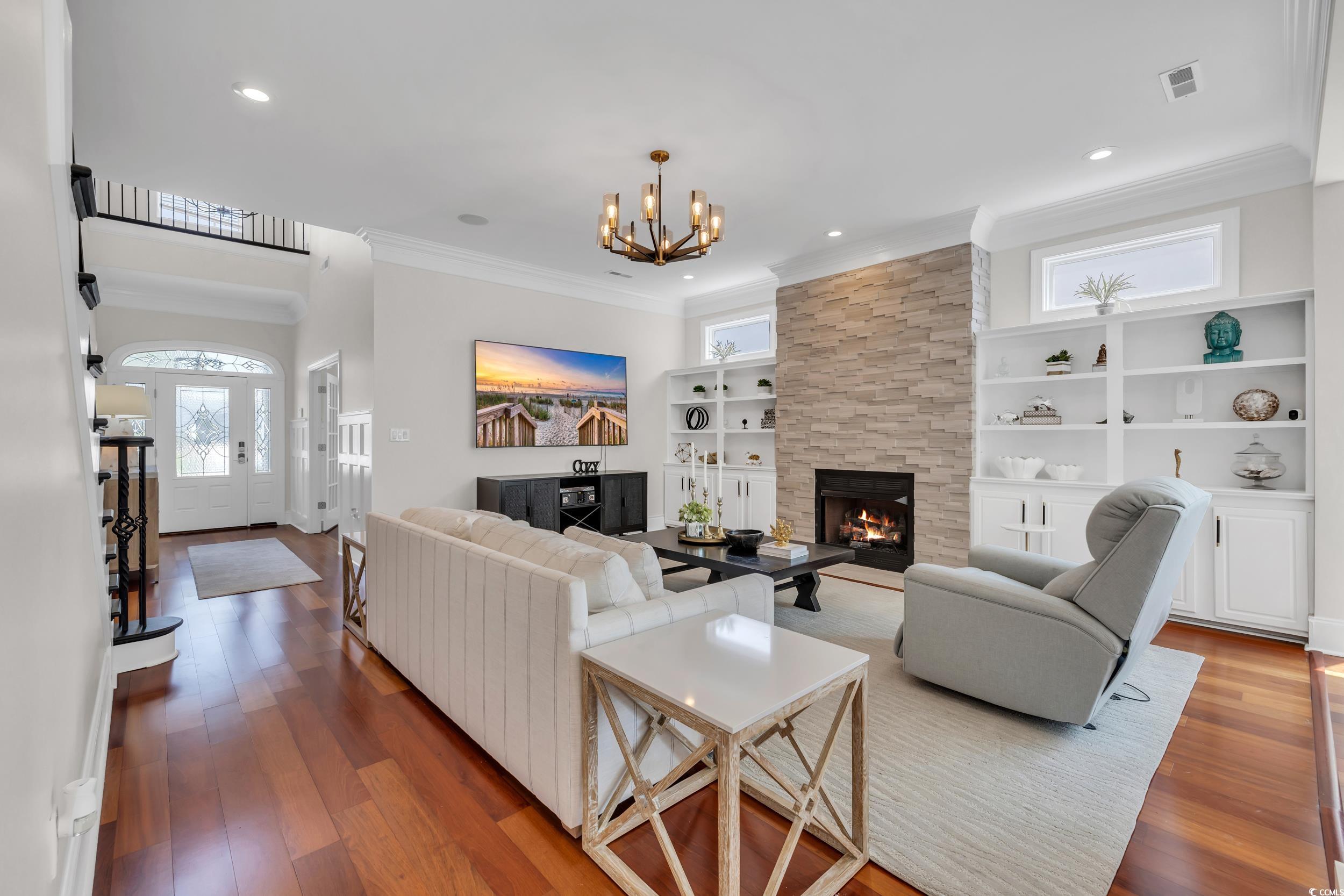 Living room with a chandelier, a fireplace, crown molding, wood finished floors, and built in features