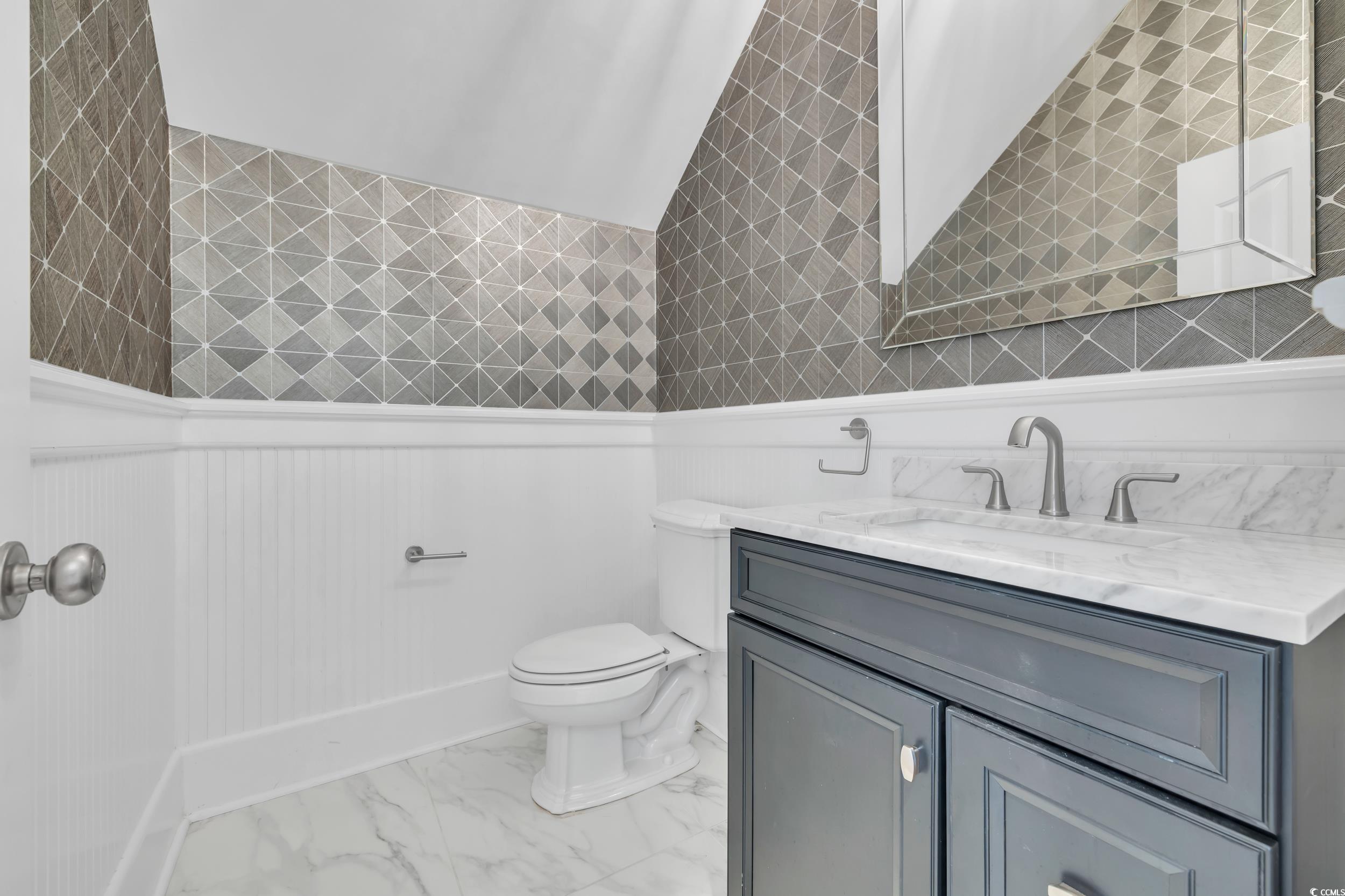 Bathroom with vanity, toilet, wainscoting, and marble look tiles