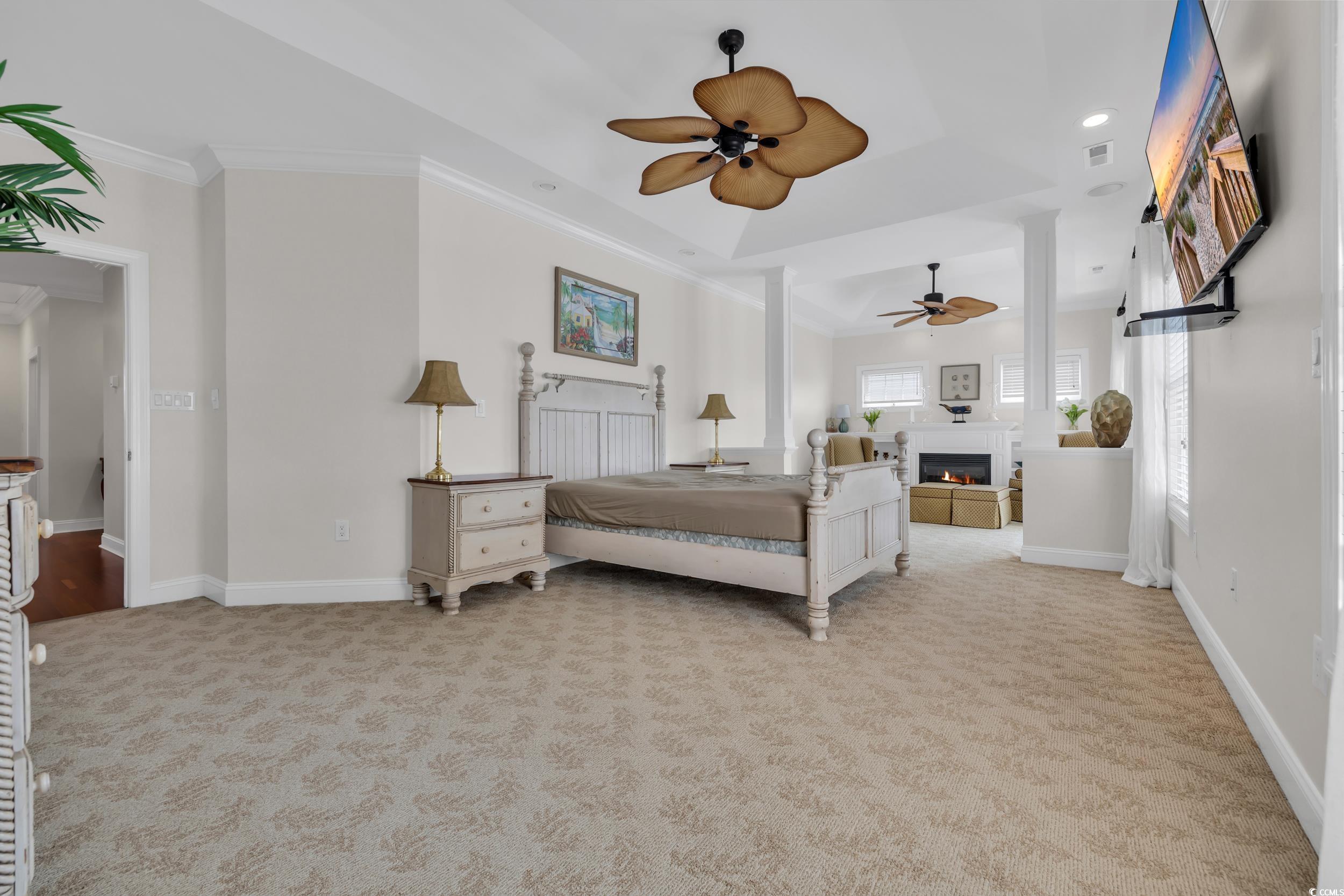 Bedroom featuring light carpet, ornamental molding, a tray ceiling, baseboards, and a glass covered fireplace