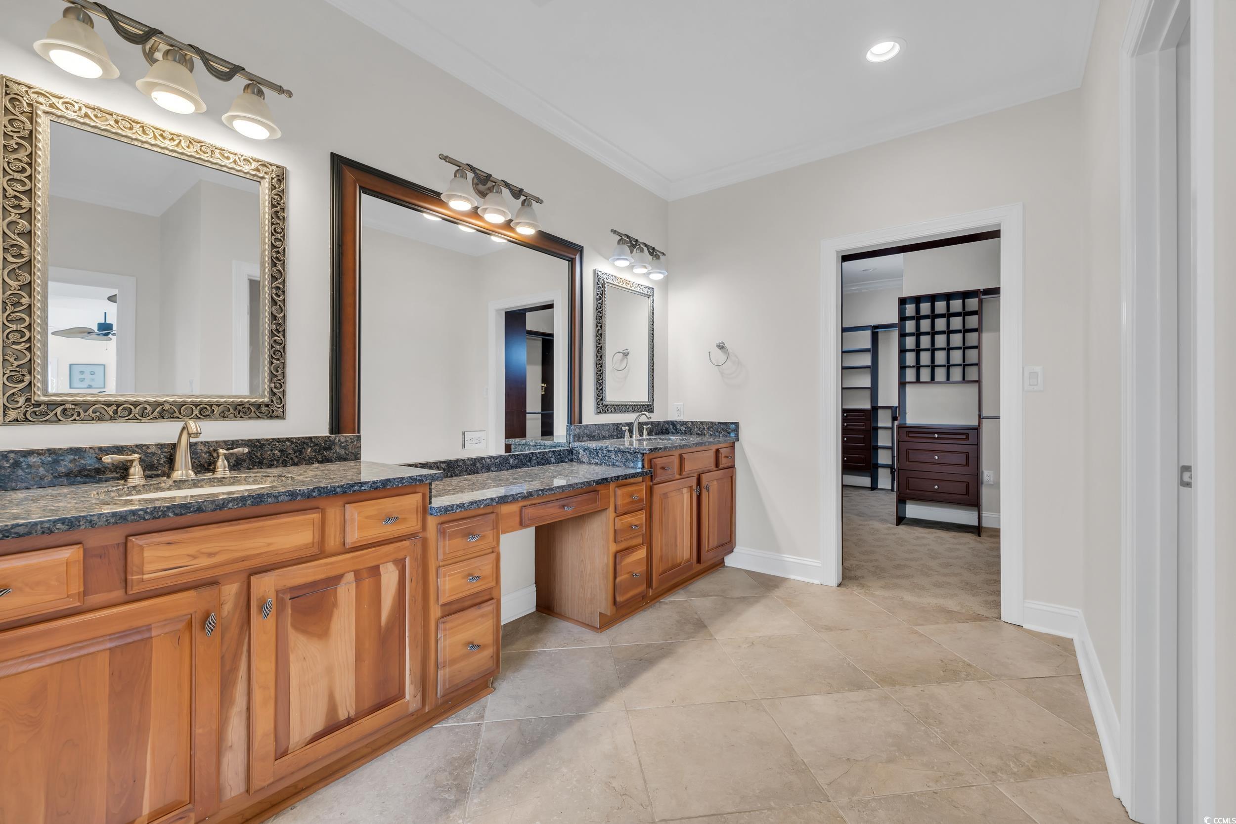 Bathroom featuring double vanity, crown molding, baseboards, and tile patterned floors