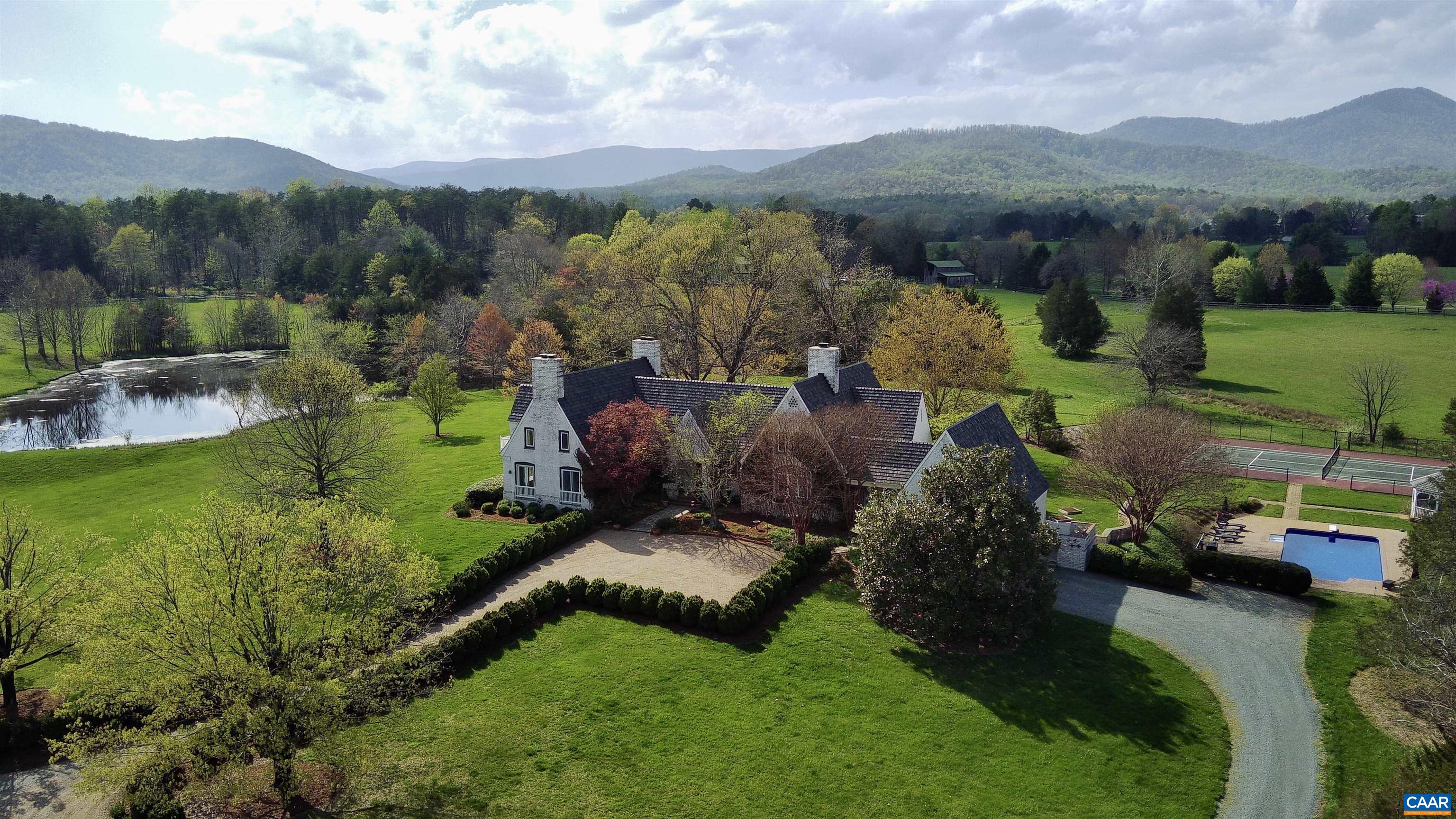 Drive under a Willow Oaks lined, canopied driveway, flanked by mountains, & enjoy the pond & pastoral views, leading to this magnificent English country estate home. Fall in love with picturesque walking trails around this unique wildlife rich property, which also features a pool, tennis/sport court, stream & barn. Entering the home, immediately fall in love with the bucolic views highlighted in the conservatory, featuring a blistered poplar wet bar. Spacious living areas with mountain views & access to private patios. The great room & kitchen feature soaring 20’ ceilings, solid Cherry hardwood floors, & hand-hewn beams, reclaimed from a 200-year-old Virginia barn. Custom built fireplace was hand laid by a local artisan.  Enjoy a kitchen designed for function, family & entertaining featuring a 11-ft granite island, Wolf induction & gas cooktop, dual KitchenAid dishwashers, 48” refrigerator. Vintage, Venetian glass doors open to the wine cellar. 1st floor & 2nd level primary bedroom options. All bedrooms have ensuite baths with access to patios & balcony views. The guest wing has two bedrooms, kitchenette, and full bathroom. New composite roof. New pool liner & cover. Room for horses! Video tour and 3D tour links avail. by request.