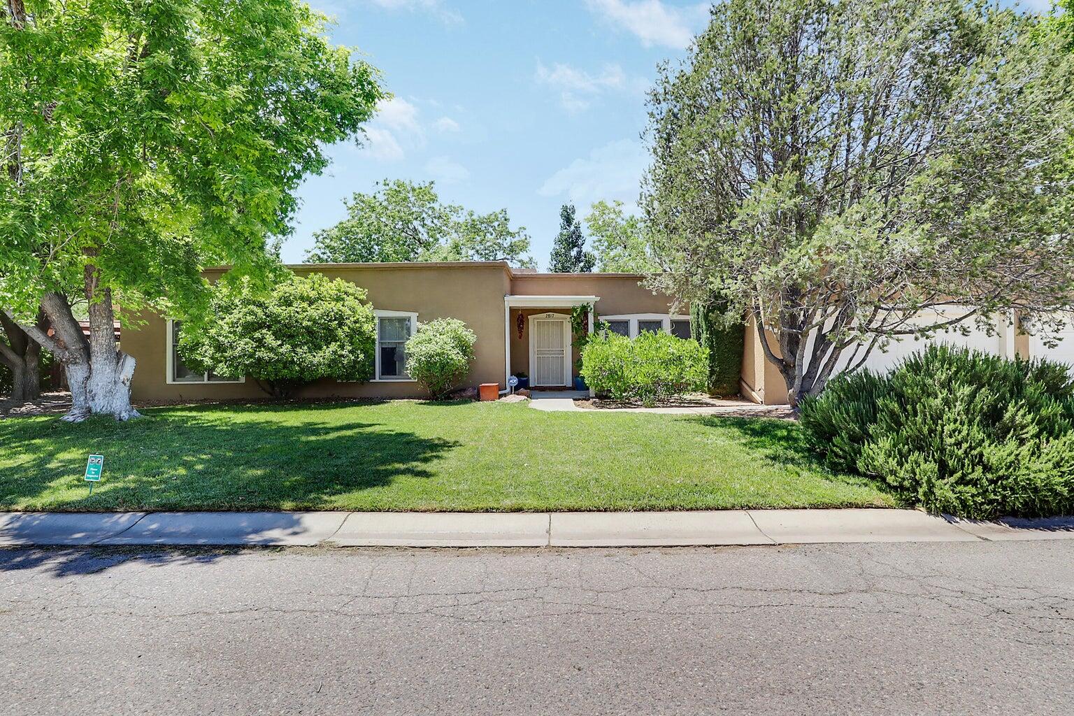 Experience timeless Southwestern charm in this beautifully updated Territorial-style home, tucked away on a quiet lane in the heart of the North Valley. Enjoy the peaceful surroundings with convenient access to the nearby acequia, perfect for walking/biking, or simply soaking in the ambiance, while being just minutes from I-40 for EZ commuting. Step inside to classic New Mexico style, featuring rich brick floors, warm wood-framed windows, and a striking stacked-stone fireplace. The thoughtfully designed kitchen includes a gas cooktop with a custom tile surround, and an island, ideal for both everyday living and entertaining. The spacious primary suite includes a cozy sitting area, a beautifully updated bath area, and a large walk-in closet. Two generously sized add'n BR's and dual living