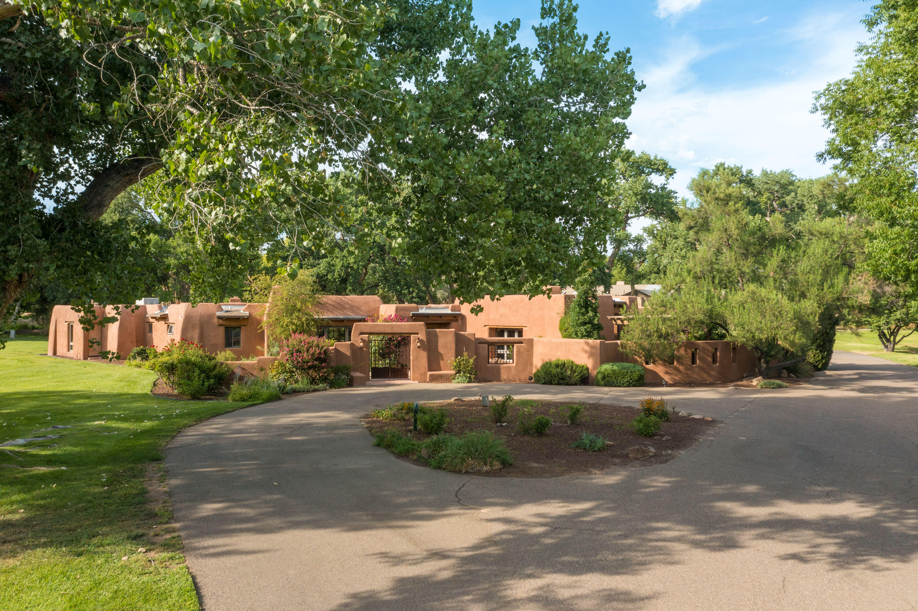 This elegant classic Calvin adobe in the heart of highly sought-after Los Poblanos sits on the prettiest 2 acre lot in the Village of Los Ranchos. A blend of history, culture and timeless beauty, this rare find has been updated for modern living. A welcoming entry opens upward to formal spaces.  Hand carved beams and softly rounded plaster walls bring that sense of peace and refuge found only within adobe structures.  Major reconstruction added a spacious family room, its high beamed ceiling and tall windows gathering light and views from every direction. Opening to the remodeled kitchen, and tableside kiva fireplace, this gathering space is magical.  The private, romantic primary suite gained a 200 sq ft walk-in closet/dressing/exercise space in the renovation, plus an accessible shower