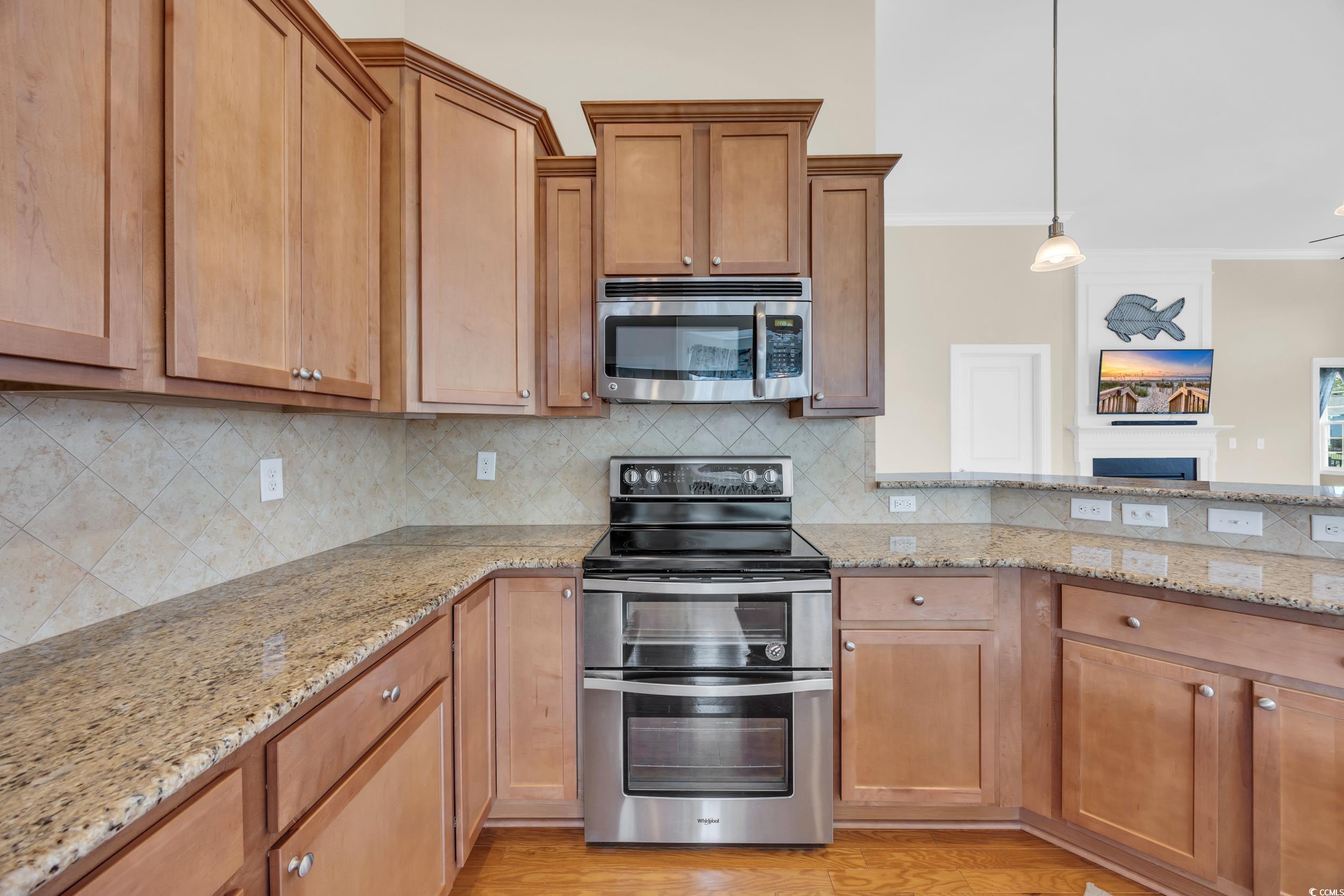 Kitchen with appliances with stainless steel finishes, backsplash, ornamental molding, light stone countertops, and hanging light fixtures