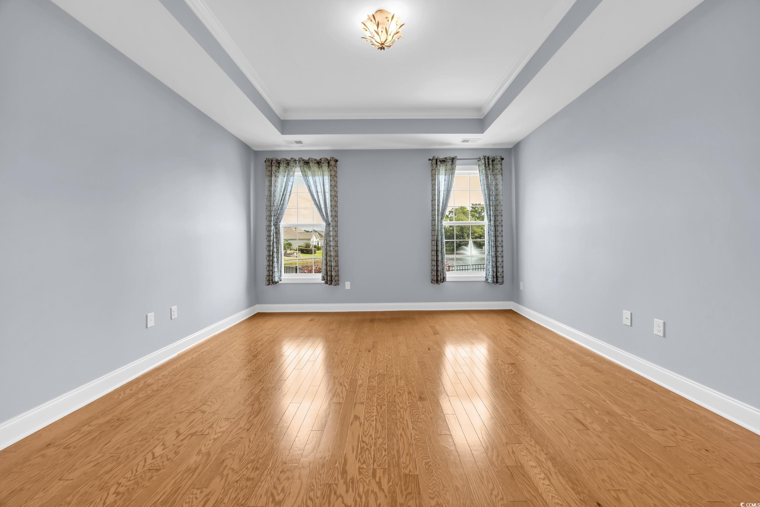 Unfurnished room featuring a raised ceiling, wood finished floors, healthy amount of natural light, and crown molding