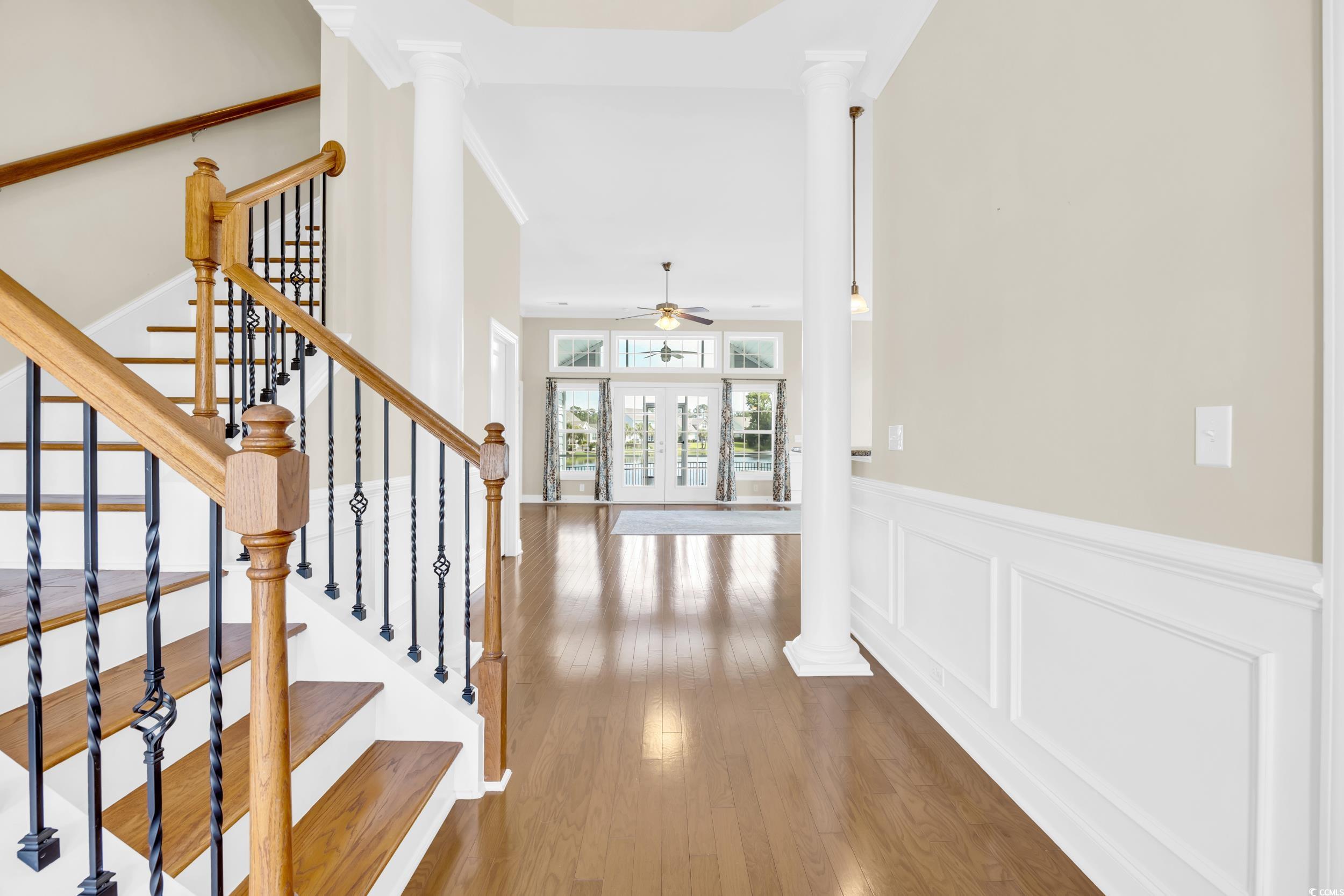 Stairway featuring ornate columns, wood finished floors, french doors, ceiling fan, and a wainscoted wall