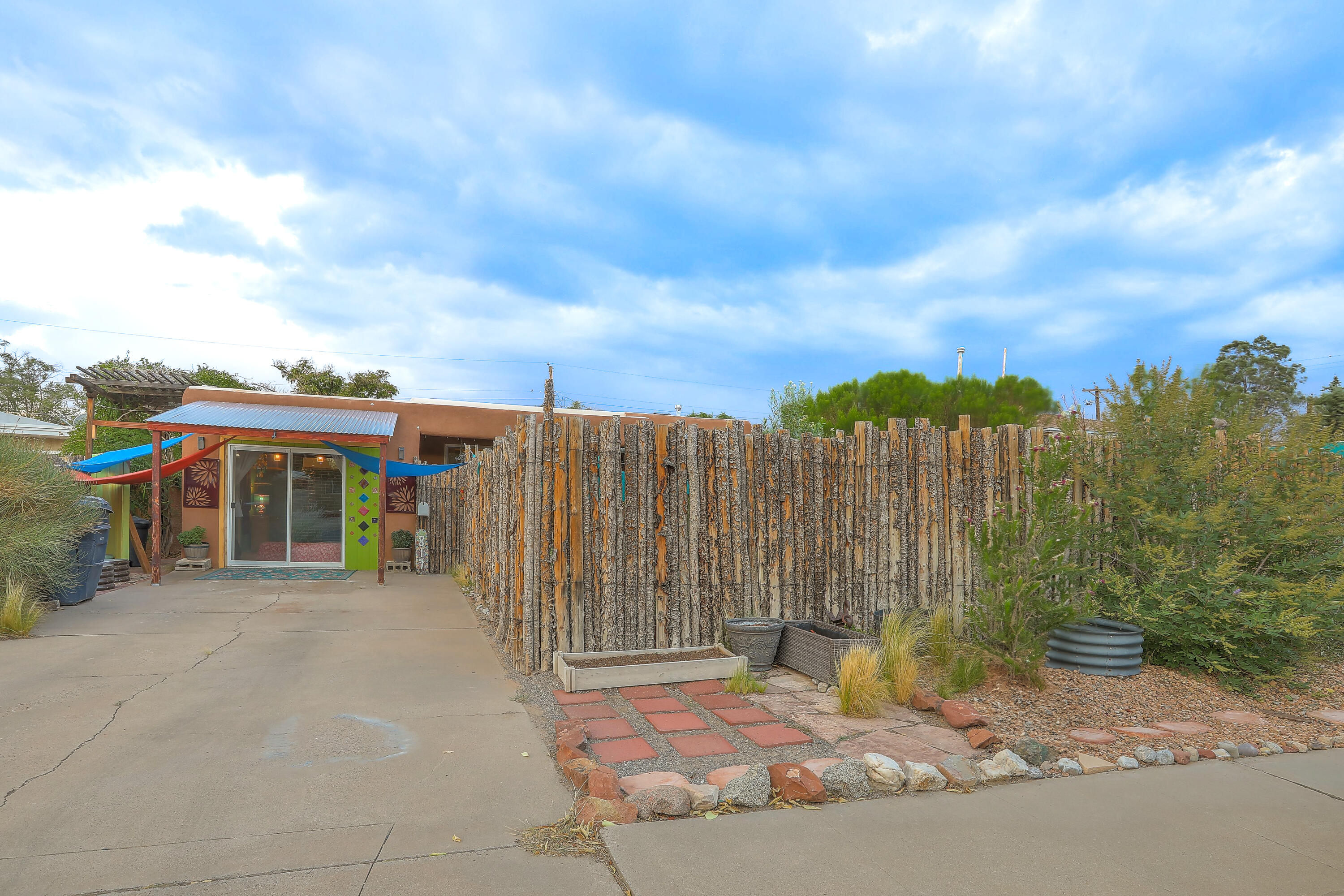 Welcome to this artist- and gardener-inspired retreat in Albuquerque's desirable Fair West neighborhood. From your front window, enjoy stunning views of the Sandia Mountains, while the fully landscaped yards offer a true urban oasis filled with color, texture, and seasonal blooms.The gardens feature a thoughtful mix of drought-tolerant and pollinator-friendly plants, including flowering perennials, ornamental grasses, and vibrant sages. Fruit trees such as fig, apple, pear, and pomegranate add beauty and bounty, while mature plantings like a 20+-year-old mimosa tree, flamethrower redbud, and climbing vines create shade, fragrance, and charm. Designed for year-round interest, the landscaping provides a private sanctuary that attracts birds, butterflies, and pollinators alike.