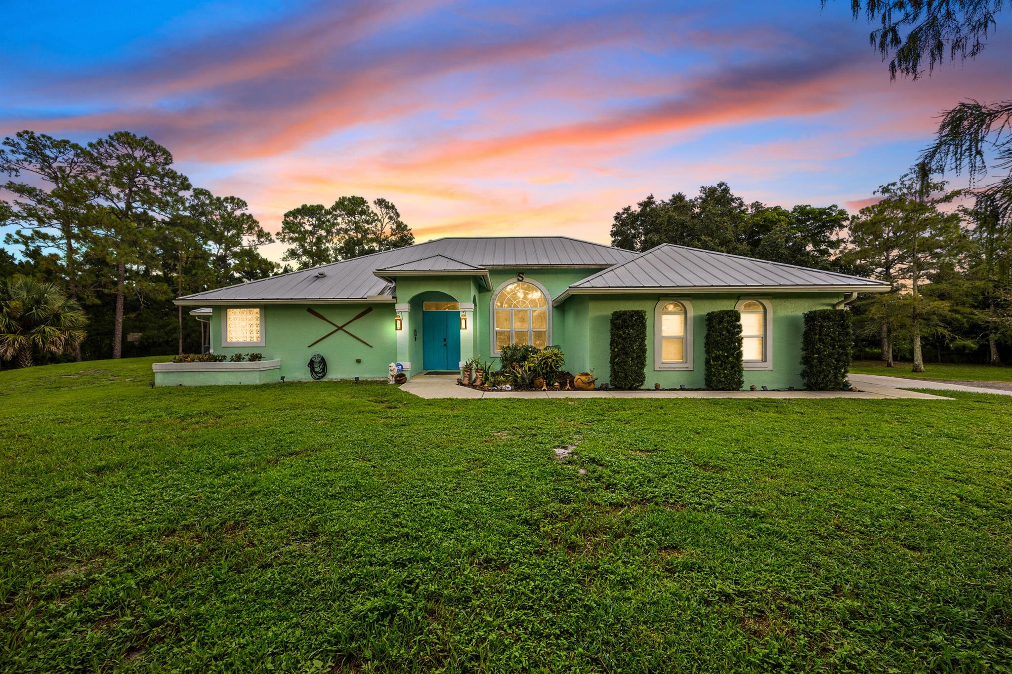 Nestled on a spacious corner lot on 1.39 acres this home exudes the quintessential Acreage lifestyle--where expansive properties meet a rural, equestrian-friendly vibe, offering residents the freedom of larger lots, proximity to nature trails, and a peaceful escape from urban hustle while still being conveniently close to West Palm Beach amenities. This stunning 3-bedroom, 2-bath main home with a 900 square foot 2 bedroom 1 bath guest house built in 2019.  The main house features a thoughtful split plan design with soaring vaulted ceilings that enhance the sense of openness and light. The heart of the home is an inviting open-concept kitchen boasting stainless steel appliances, seamlessly flowing into the living and dining areas--ideal for modern family living and entertaining. The master suite is a private retreat, complete with a luxurious bath featuring a separate shower and indulgent soaking tub, plus a spacious walk-in closet. Additional conveniences include a 2-car garage and a durable standing seam roof. Step outside to your personal oasis: a sparkling pool surrounded by an expansive travertine tile deck, perfect for sun-soaked gatherings. The fully fenced property also includes a tranquil pond with a charming dock, inviting relaxation amid lush greenery.
Adding to its appeal, the detached 900 sq ft guest house&#x14;offering 2 bedrooms and 1 bath&#x14;is currently rented month-to-month for $2,500, providing excellent income potential or space for extended family. With its vibrant outdoor spaces, including a tiki-style patio and thematic decor, this property isn't just a home; it's a lifestyle haven in The Acreage, where you can embrace outdoor adventures, gardening, or simply the joy of wide-open spaces. Don't miss this unique opportunity to own a slice of Florida paradise!