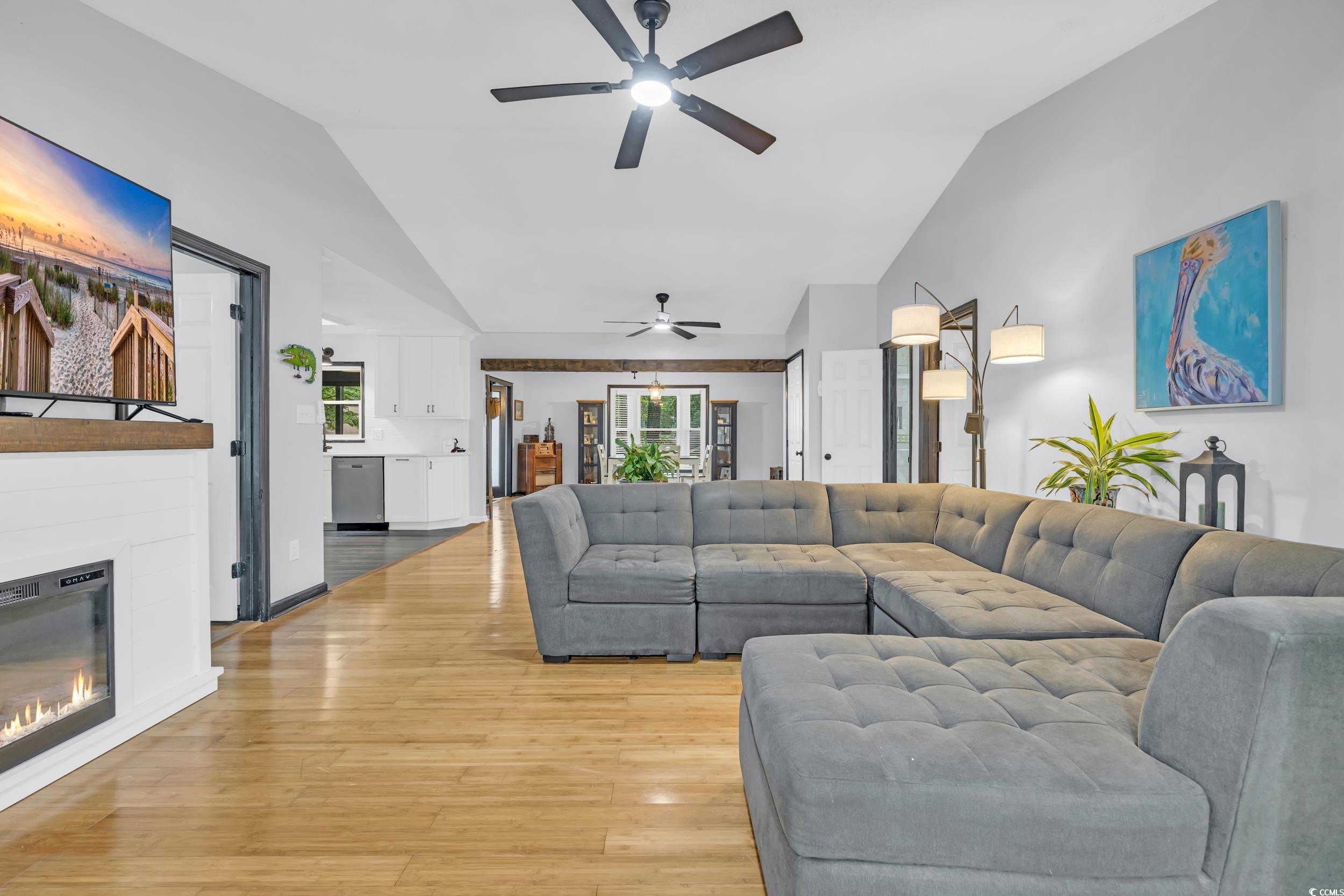 Living room with a glass covered fireplace, light wood-style floors, lofted ceiling, and a ceiling fan