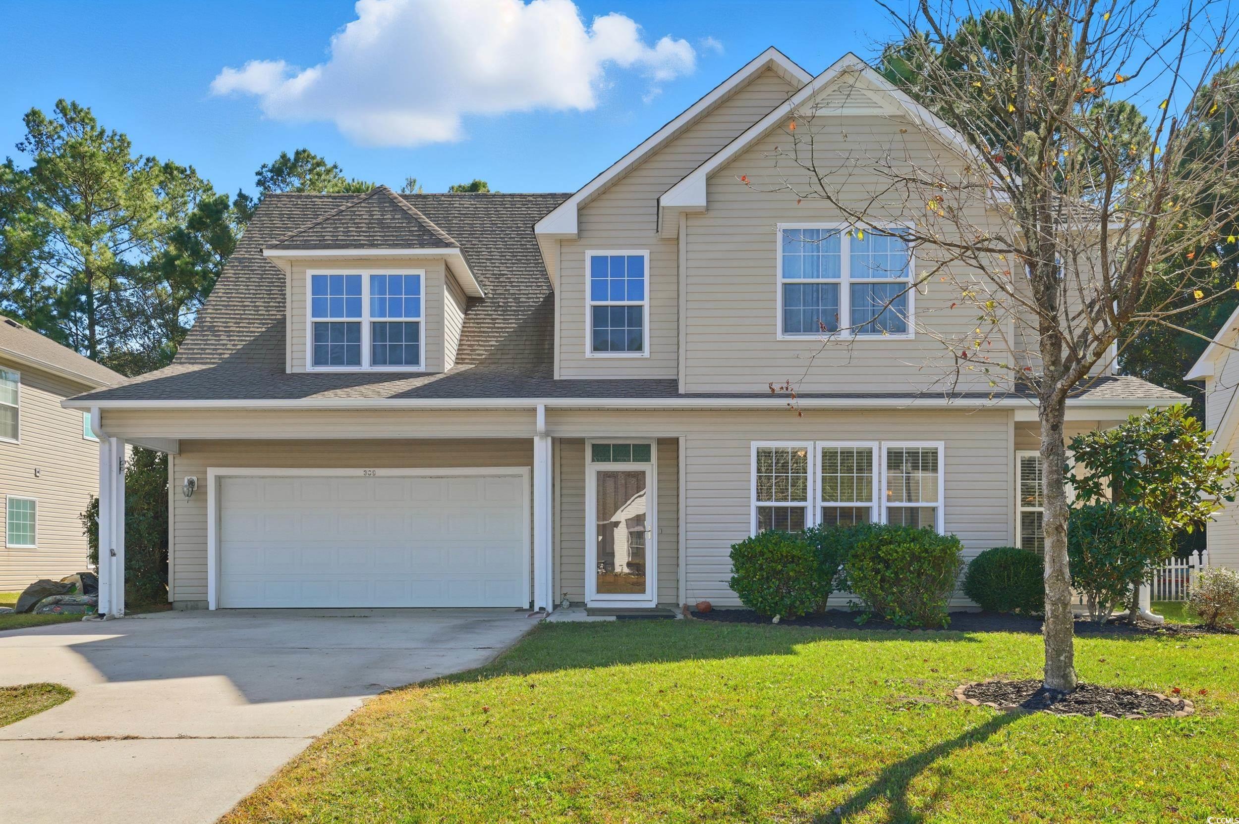 Traditional-style house featuring concrete driveway, a shingled roof, a front yard, and a garage