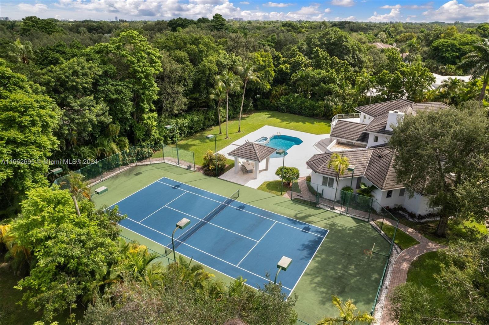 Spacious 9,018 SF, 6-BD, 5.5-BA contemporary residence on a sprawling acre-plus lot in coveted North Pinecrest area. The carefully curated layout offers modern elegance, volume ceilings, and natural light through oversized windows. The expansive eat-in kitchen has custom cabinetry, large center island, premium appliances, and pantry. The backyard features a spacious covered terrace, sparkling saltwater pool with waterfall jacuzzi, wet bar, and newly resurfaced lighted tennis court, in lush manicured grounds with mature trees providing optimal privacy. Additional features include impact windows and doors, smart home system, new staircase, fireplace, ample parking, and insulated 2-car garage with epoxy flooring and AC.