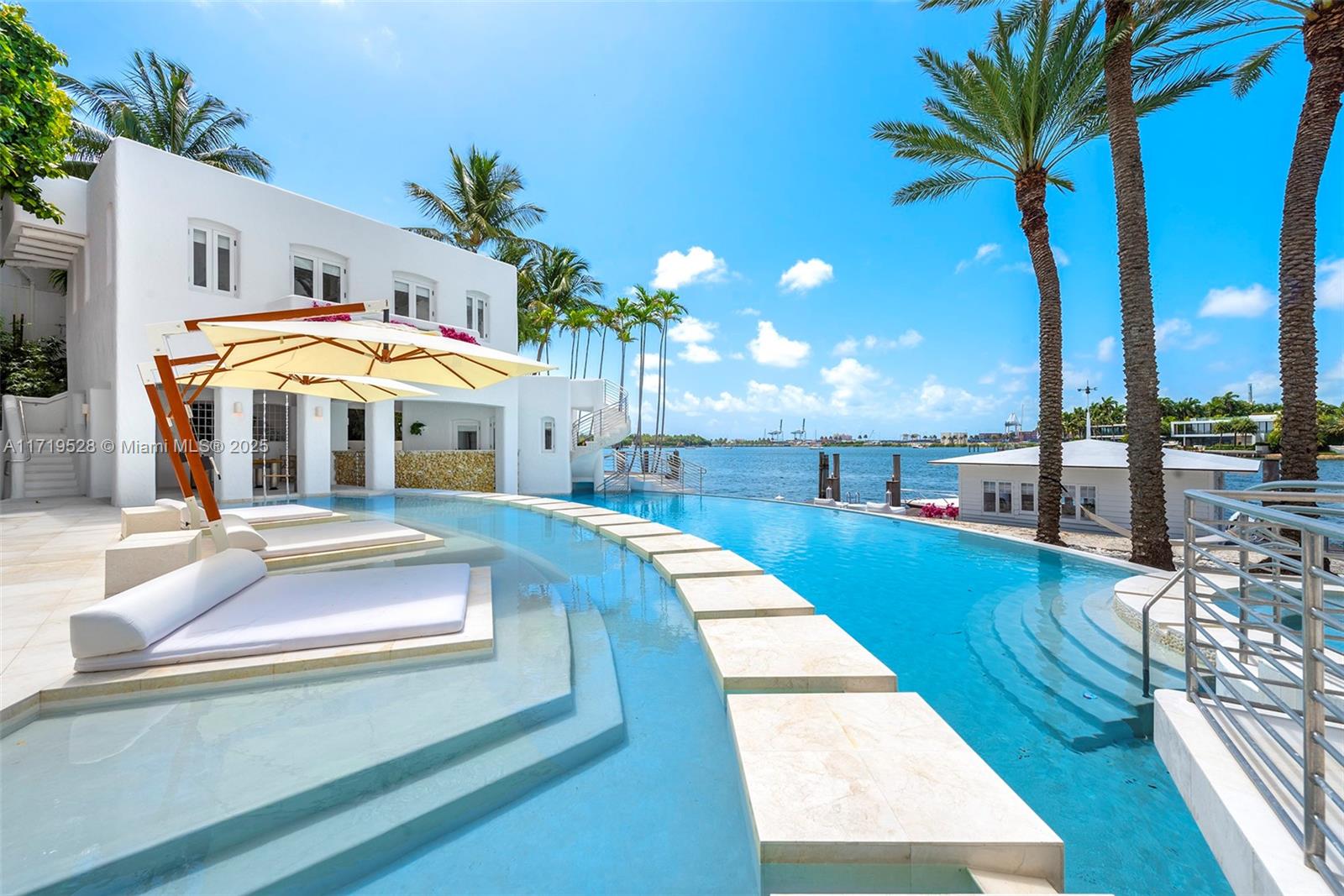 This Mykonos-inspired masterpiece, owned by former Ferrari F1 driver Eddie Irvine, redefines luxury island living. Featured in design magazines, this 13,000+ sqft estate offers 7 bedrooms, 7.5 bathrooms, detached guest suites, and Miami’s only over-water dock house. Highlights include a two-level pool, a stone footbridge and a three (now outlawed) staircases that descend into the water. Expansive rooftop terraces and a watchtower showcase the stunning southeast-facing views and 150 feet of pristine water frontage. Located on guard-gated Hibiscus Island which features family-friendly amenities including tennis & basketball courts, one of the most highly sought after locations in Miami Beach.