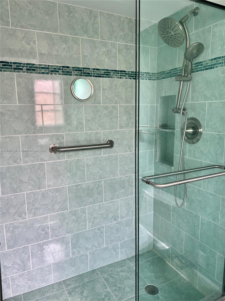 Updated primary walk-in shower featuring beautiful tile work, glass tile border and grab bar.